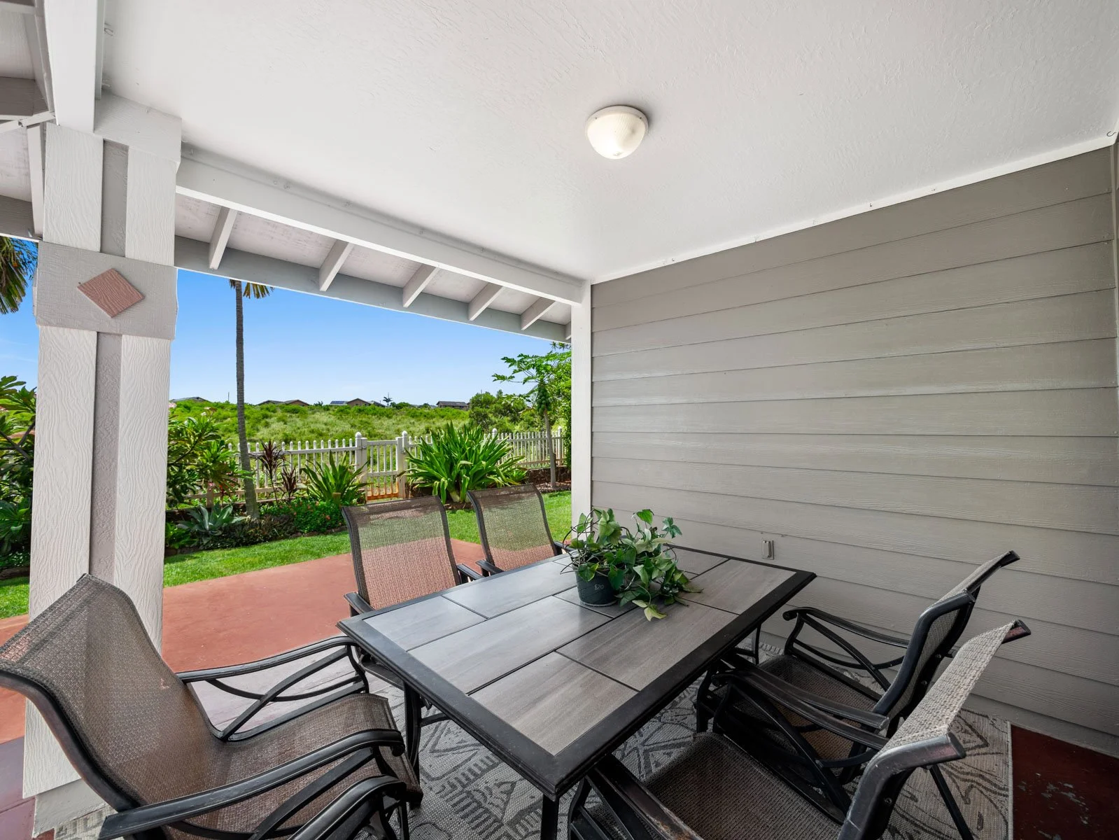 Covered lanai with outdoor dining table and view past the fence line