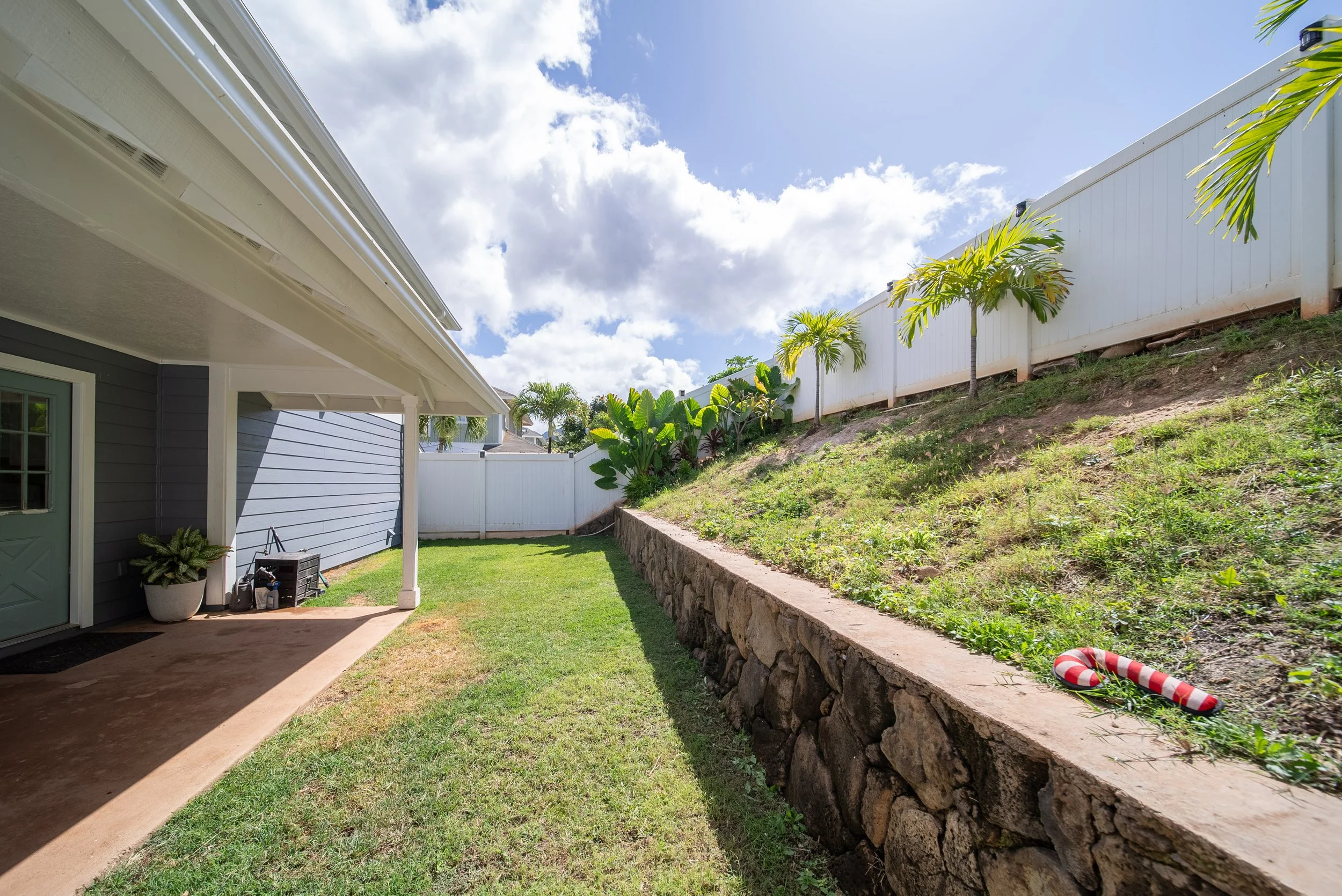 Side yard with lawn, rock retaining wall and young palms, Maili Sea Palekai