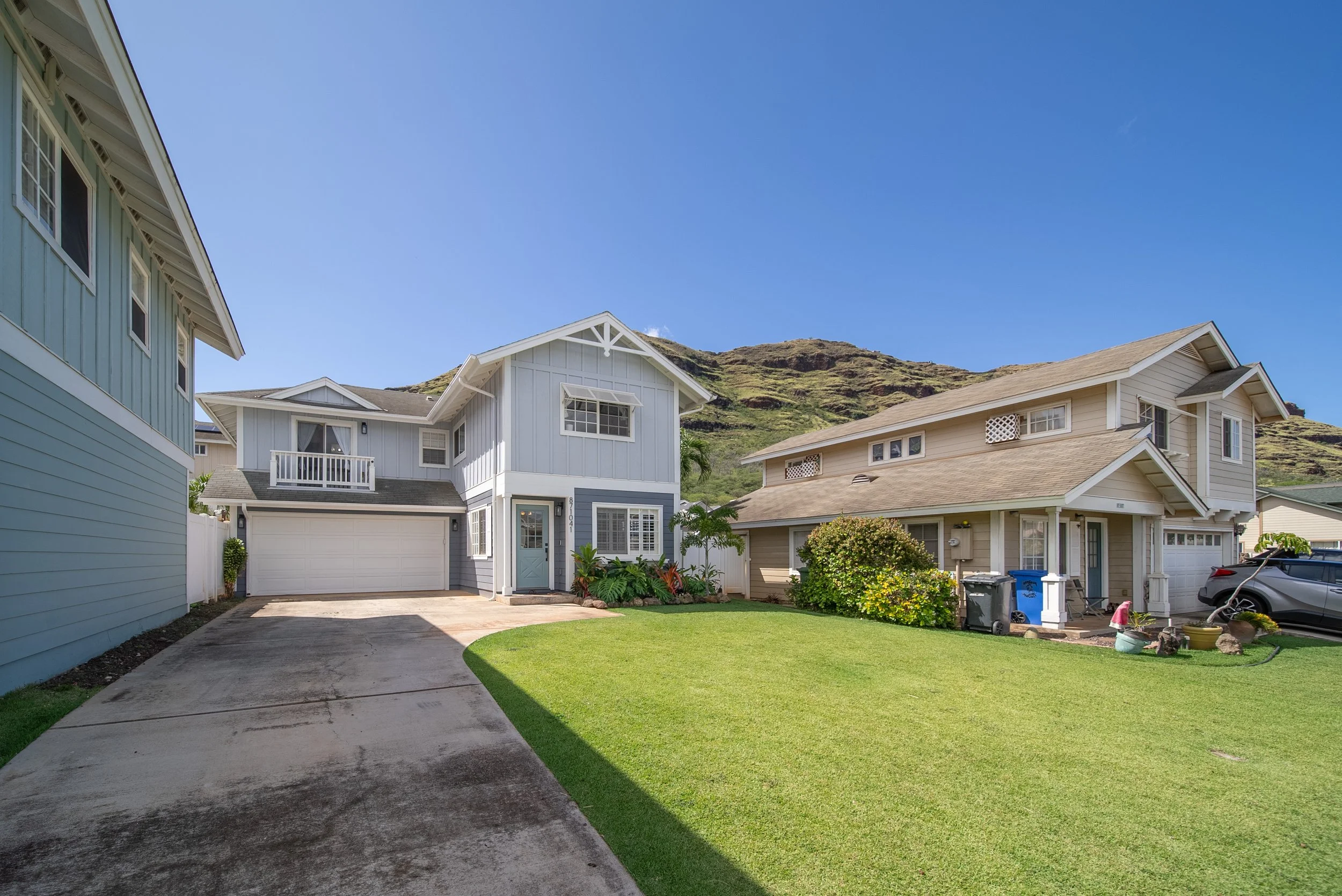 Front exterior with driveway and lawn, mountain ridge rising behind, Waianae