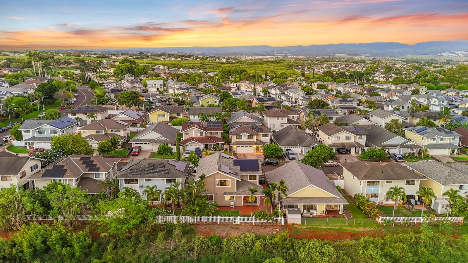 Aerial at sunset over Royal Kunia rooftops toward the mountains