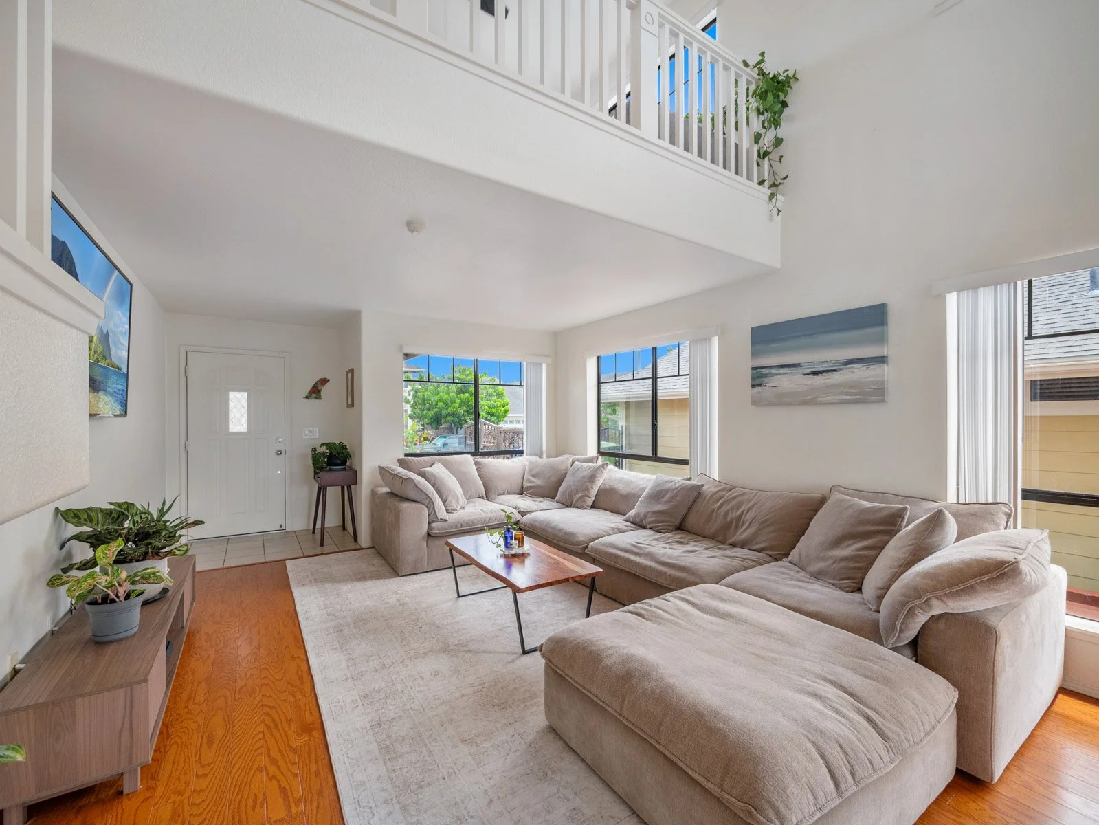 Two story living room with sectional, loft railing above and entry door