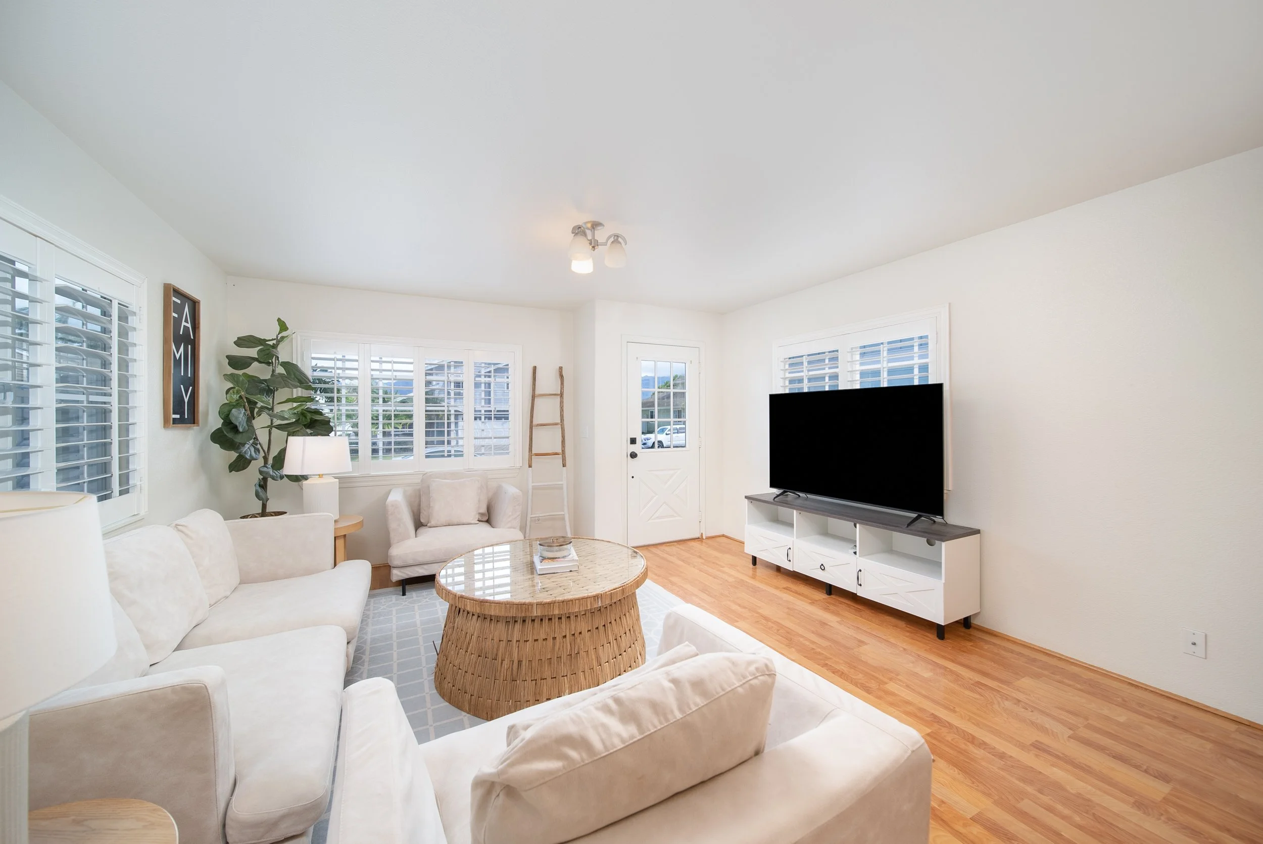 Bright living room with white sectional, plantation shutters and wood floors