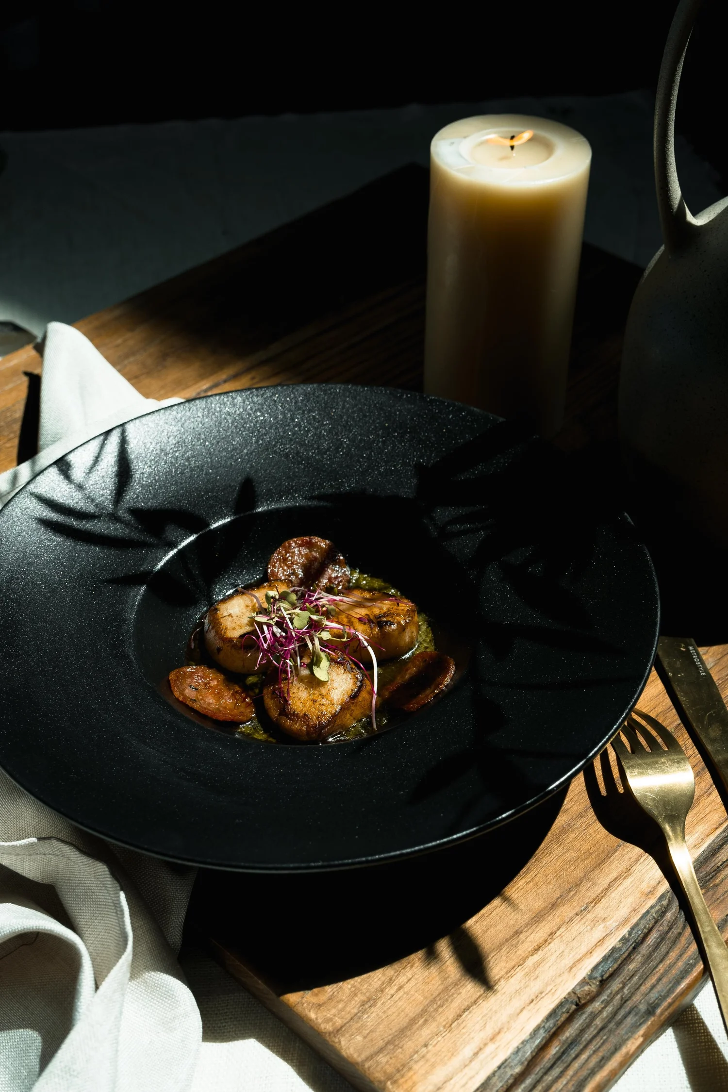 A carefully composed dish in a dark ceramic bowl beside candlelight