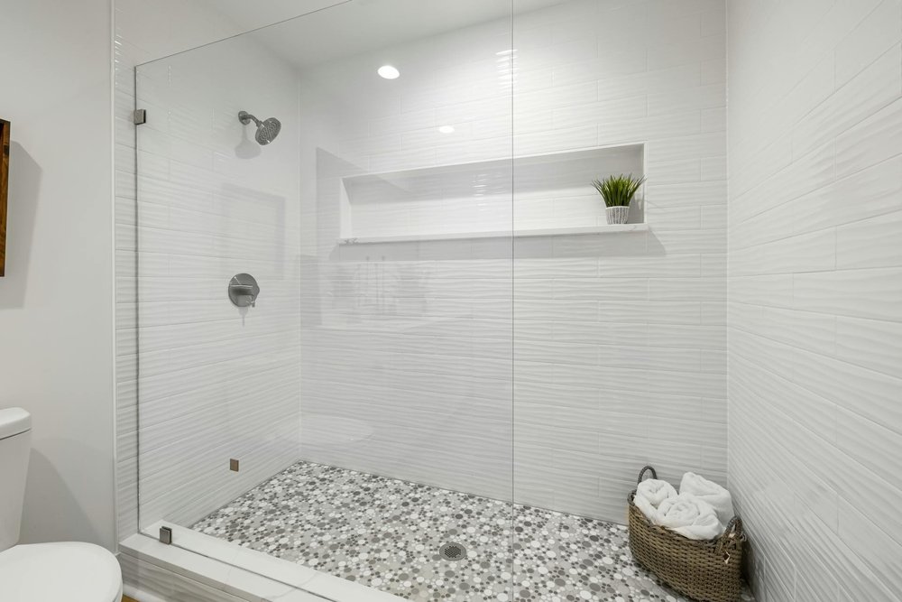 White textured shower tile with a wide recessed niche, glass enclosure and mosaic tile floor