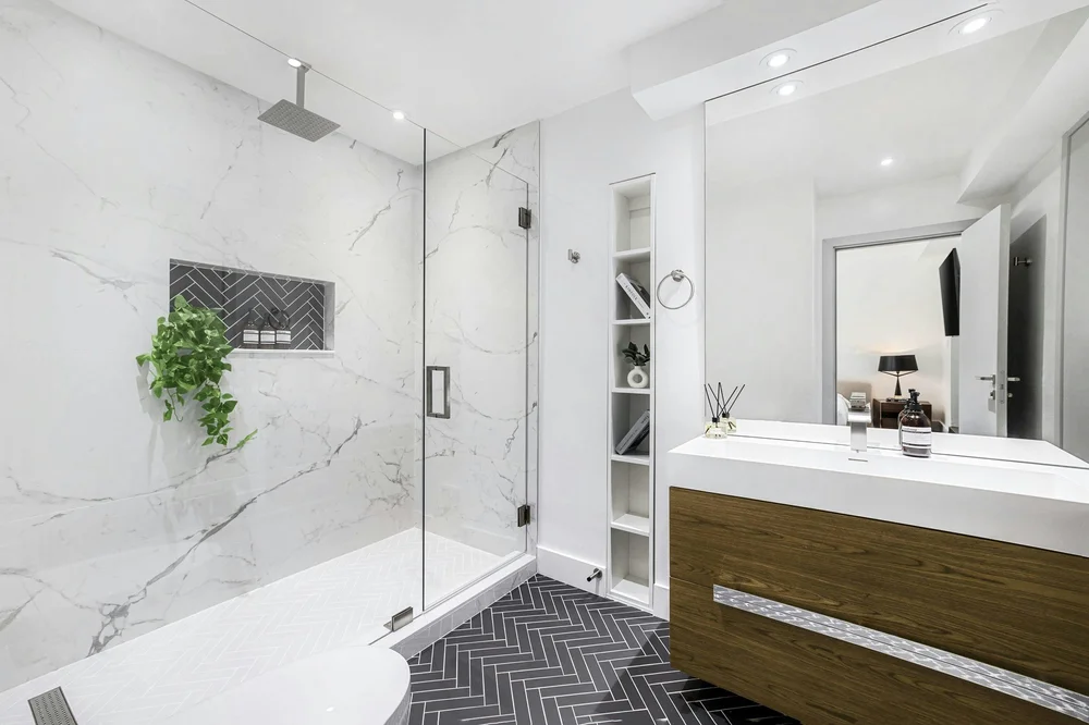 Marble-look shower tile with a herringbone niche, dark herringbone floor and wood vanity