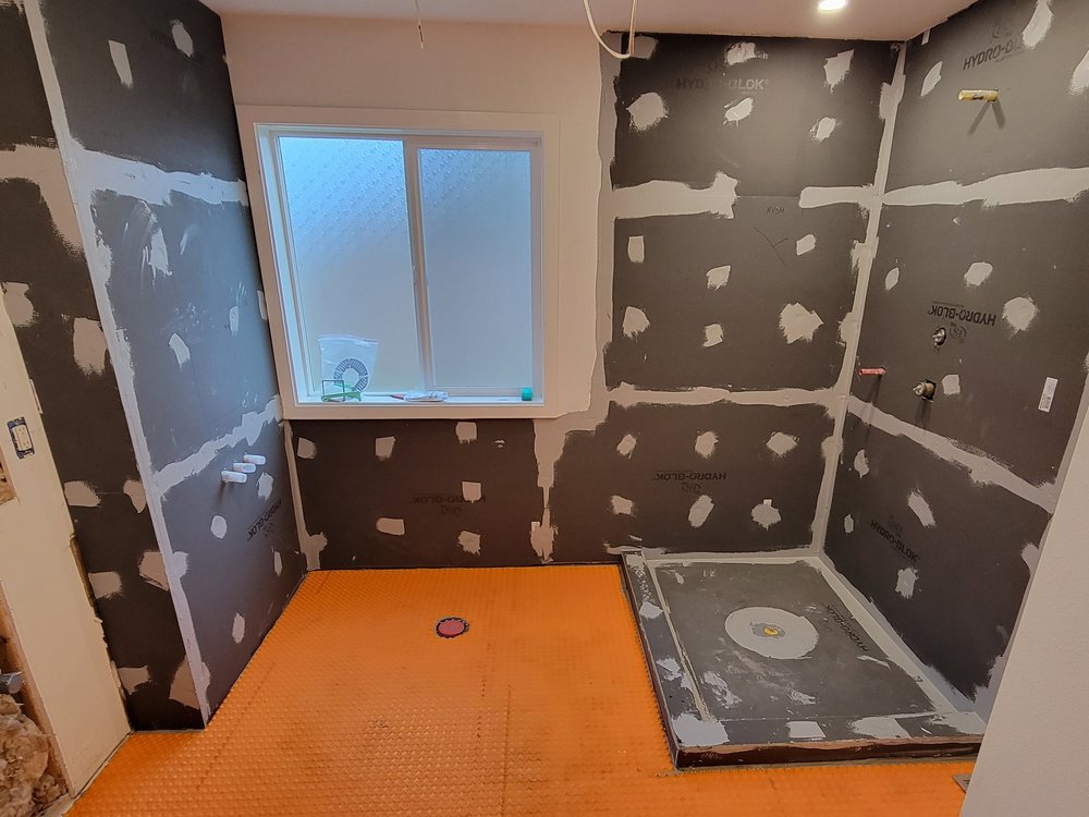 Shower preparation with wall panels, sealed seams, orange floor covering and a shower base on the right
