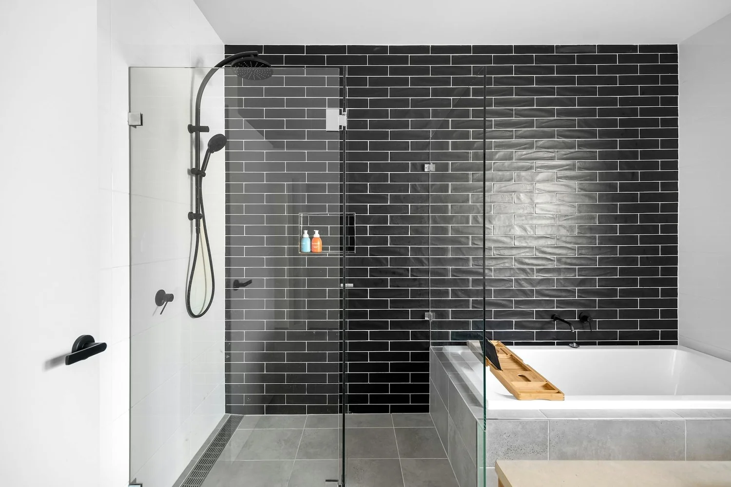 Glass shower enclosure with black subway tile, rainfall shower and pale tiled floor