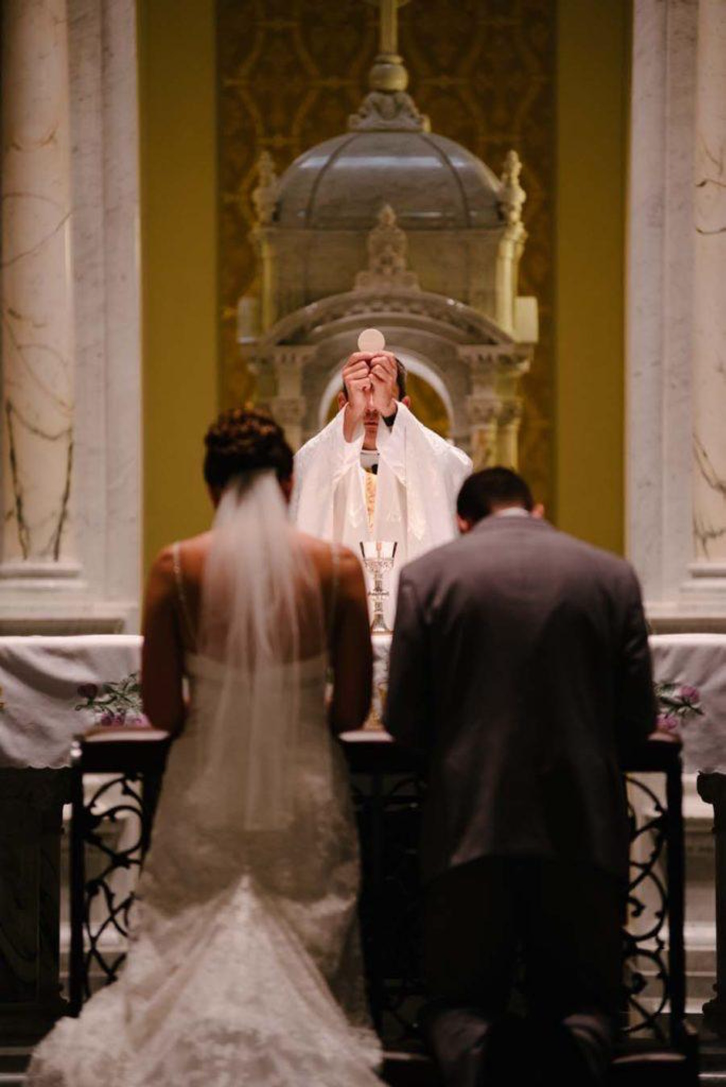 Bride and groom kneeling at the altar, priest elevating the Eucharist