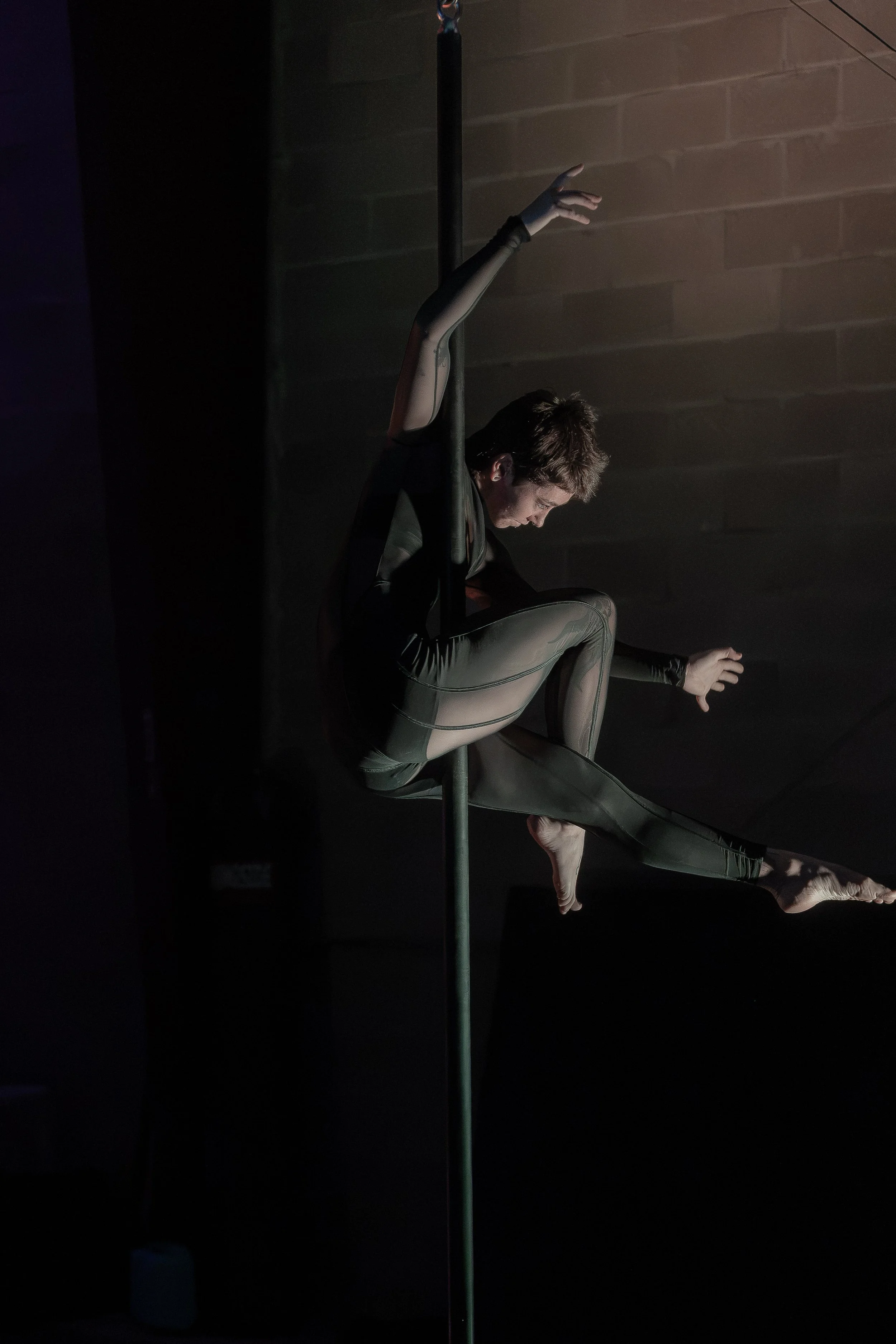 Aerialist gripping a suspended fly pole with legs extended