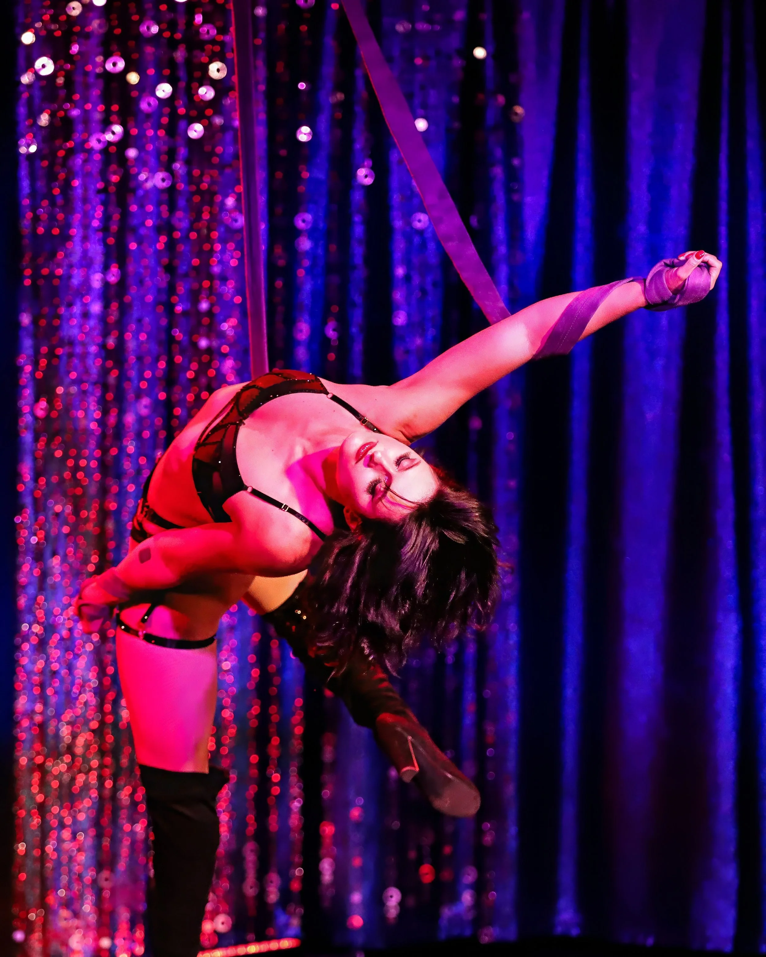 Aerialist arching back on aerial straps under purple stage light