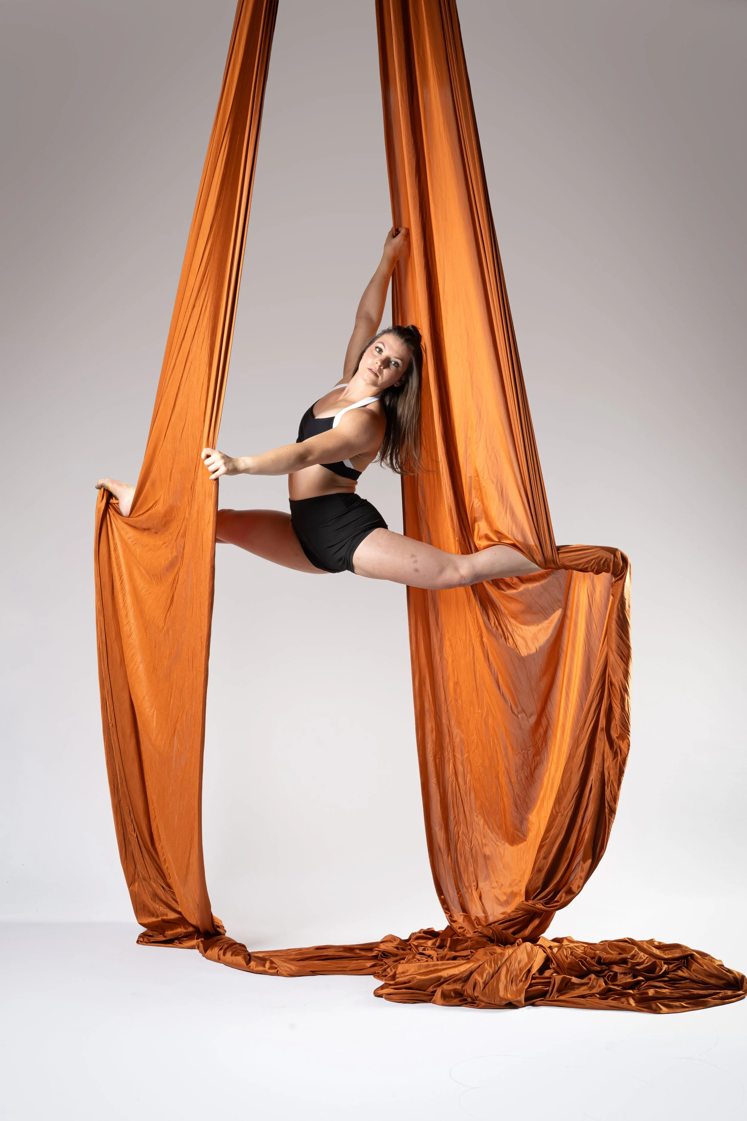 Aerialist holding a split between two lengths of copper aerial silk