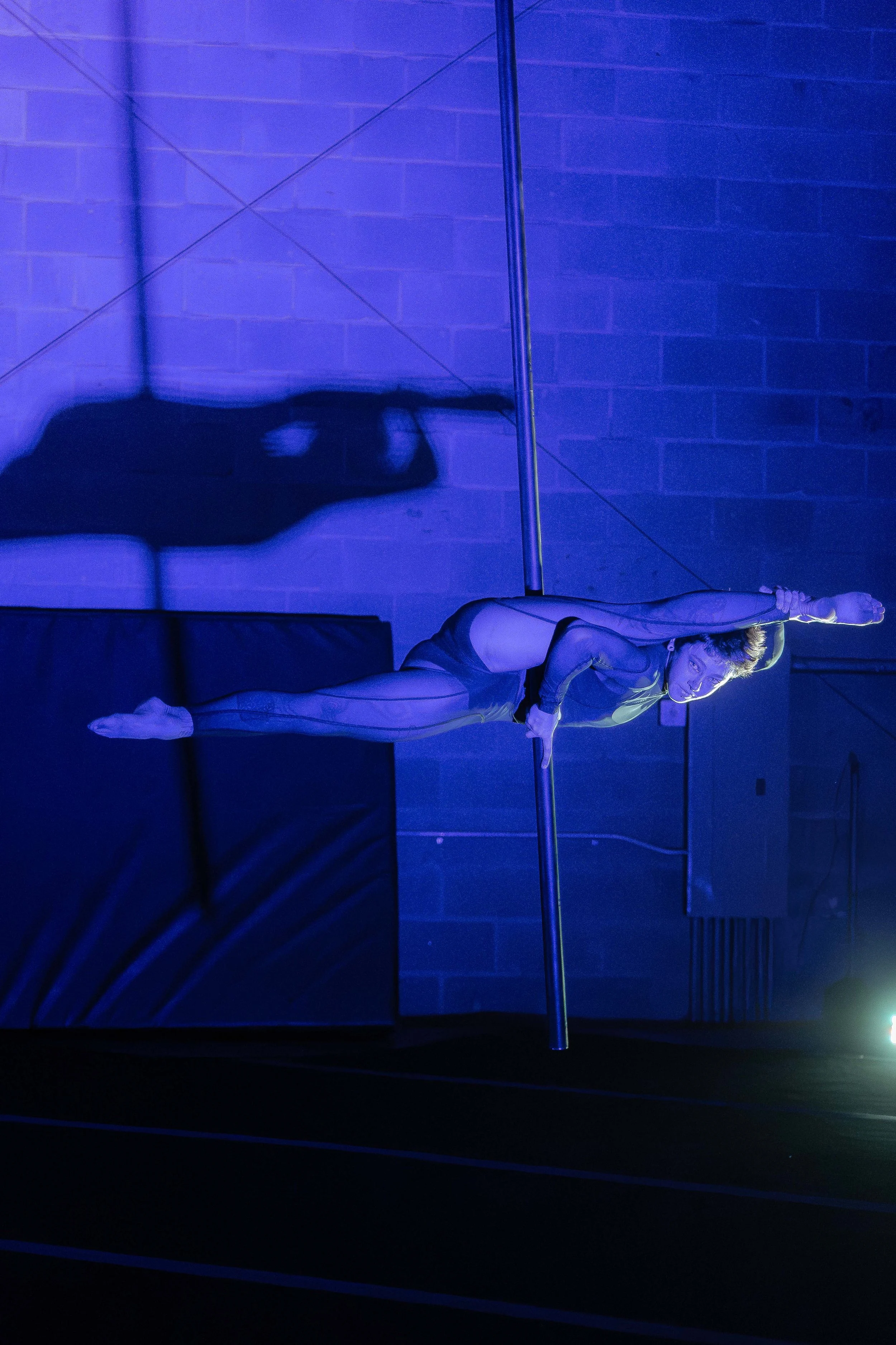 Aerialist holding a horizontal flag on a fly pole under blue light