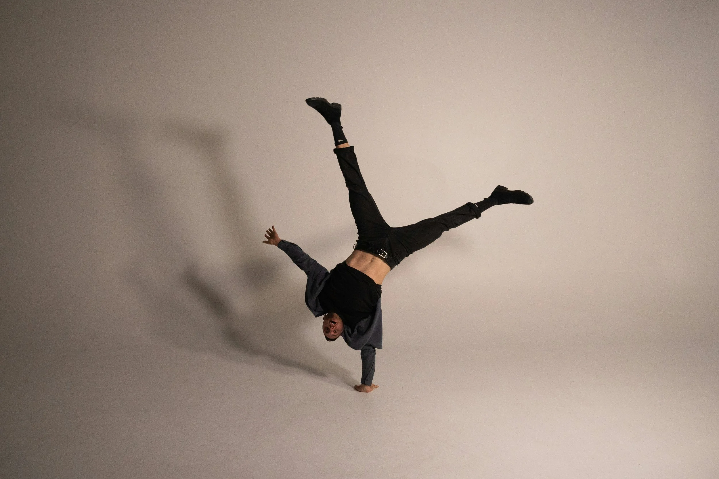 Acrobat balancing on one hand in a cartwheel shape, legs split overhead