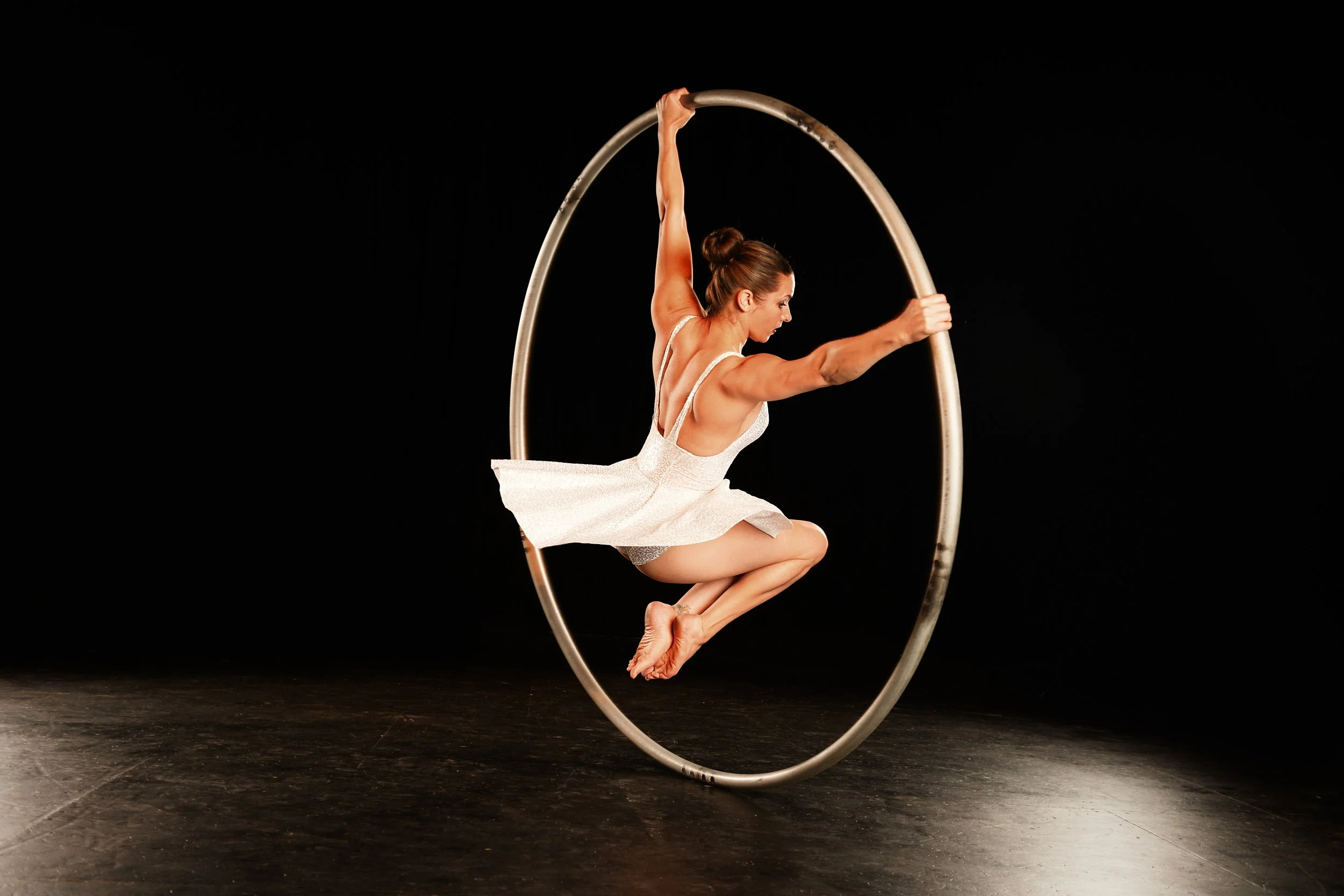 Nicole Londraville riding inside a cyr wheel against a black background