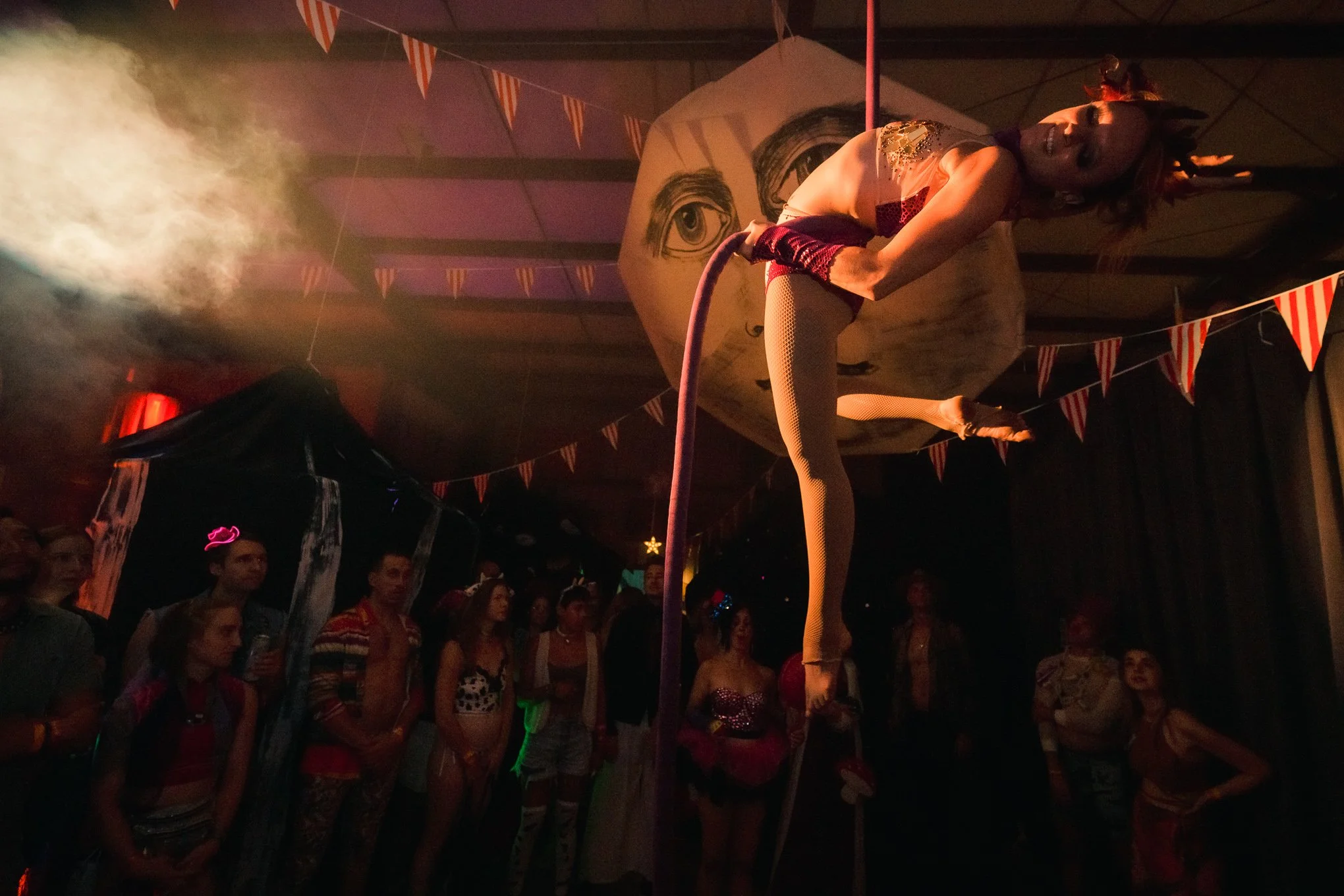 Aerialist posing on a rope above a crowd at a circus-themed party