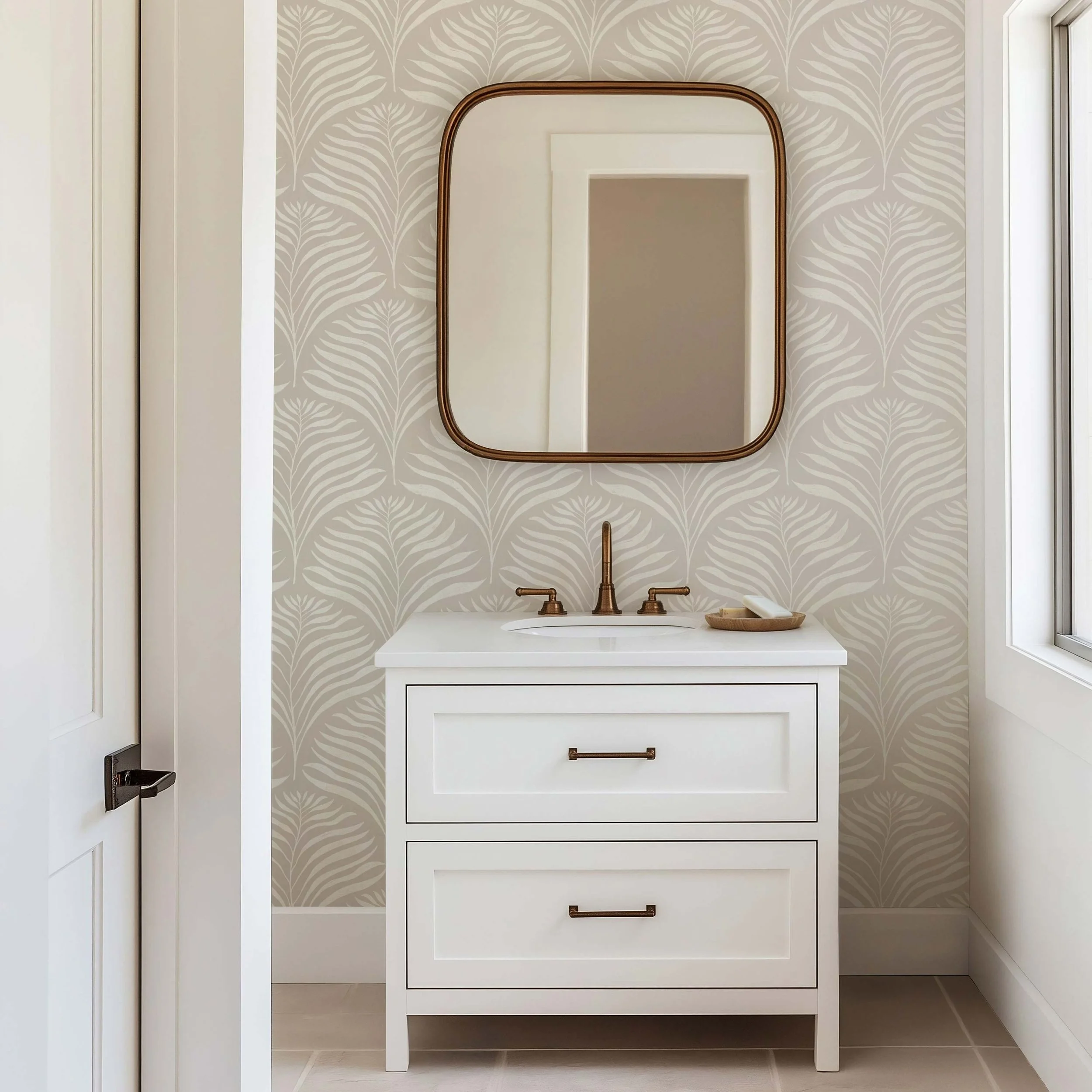 Neutral beige and cream palm leaf wallpaper for a modern minimalist bathroom, styled with a white vanity, brass fixtures and a vintage-inspired mirror.