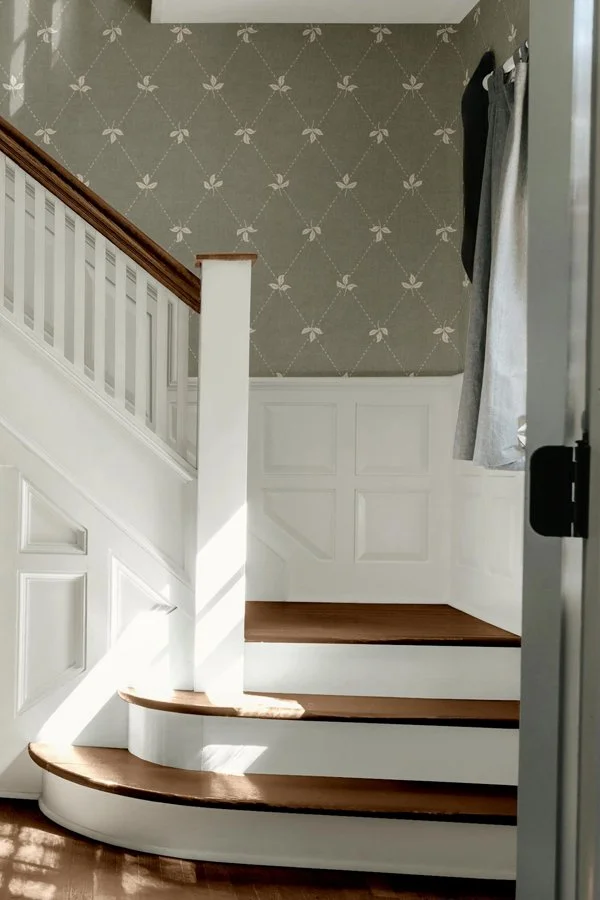 Calm botanical wallpaper featured in a traditional entryway with a staircase and timeless interior details.