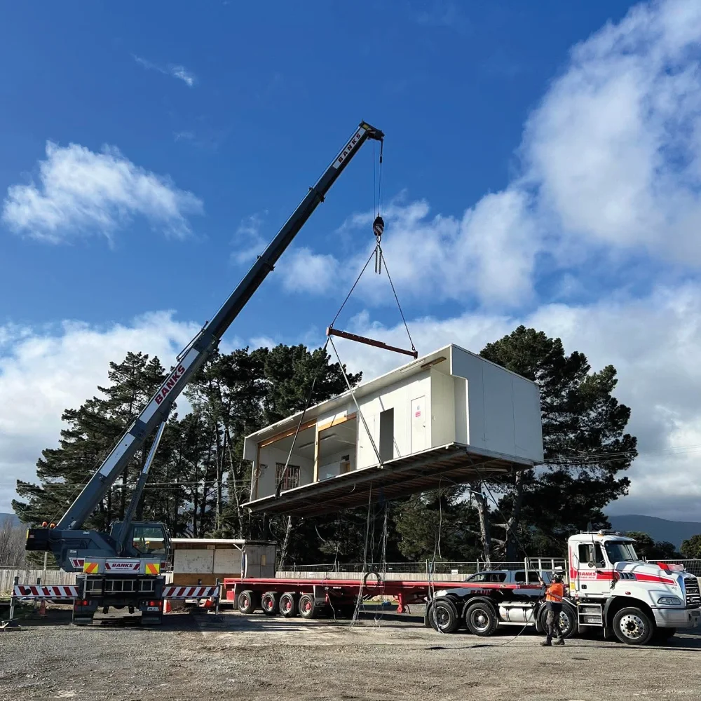 Banks Crane and Transport mobile crane lifting a portable building from a transport trailer for final placement.