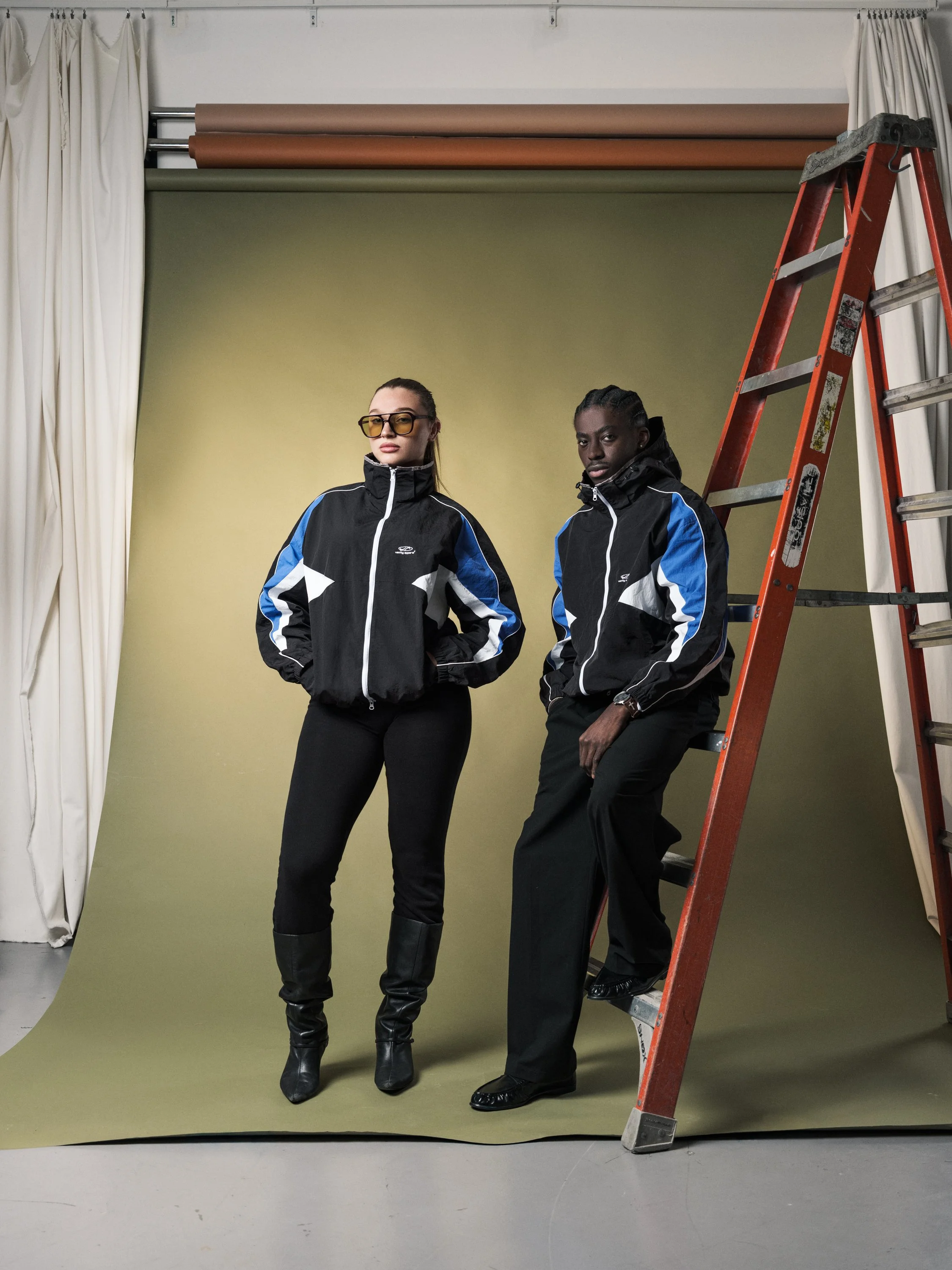 Vanity Apparel advertising image with two models styled in black jackets beside a studio ladder