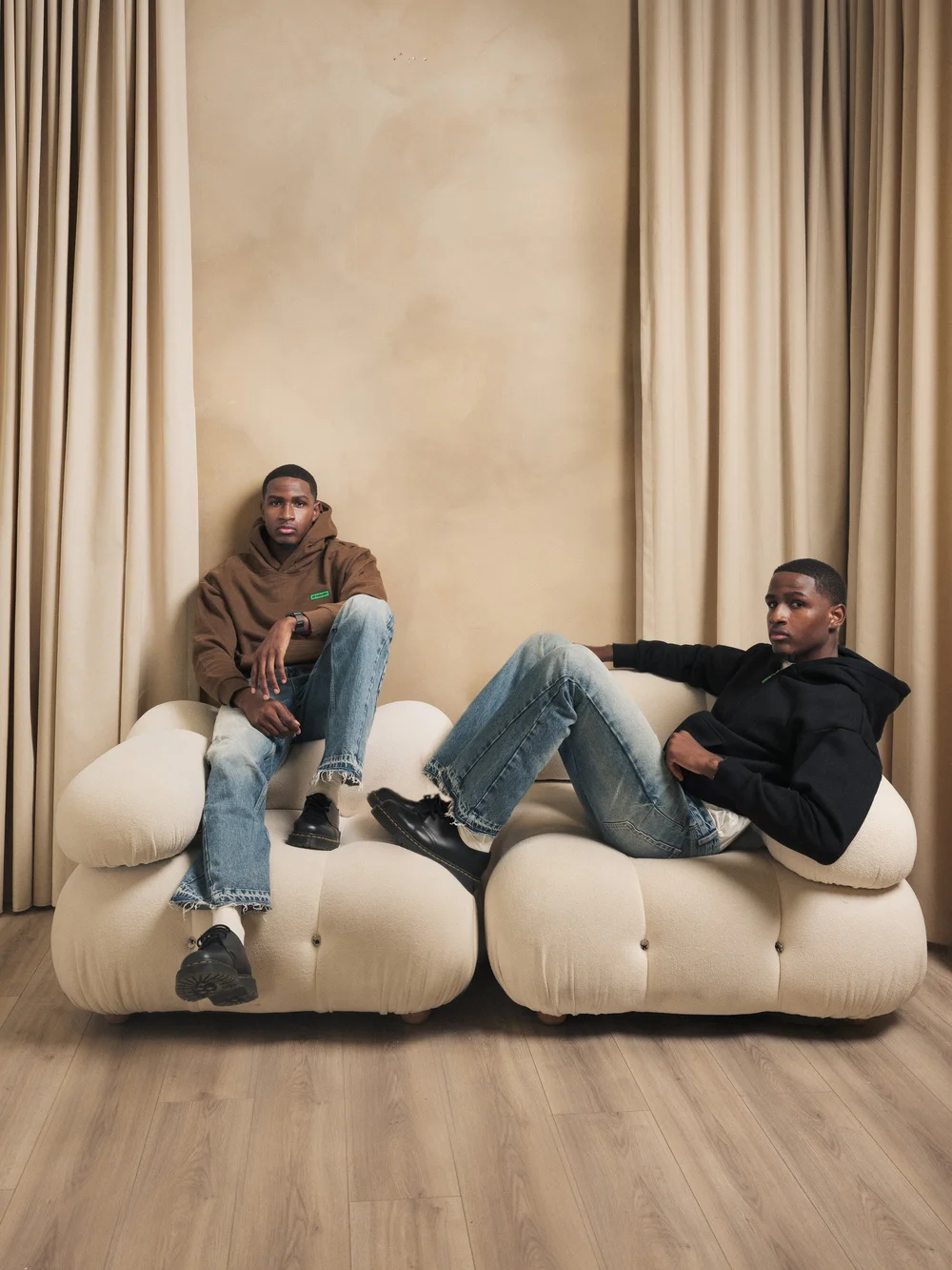 Two models in R3 CONCEPT hoodies seated on a cream sofa