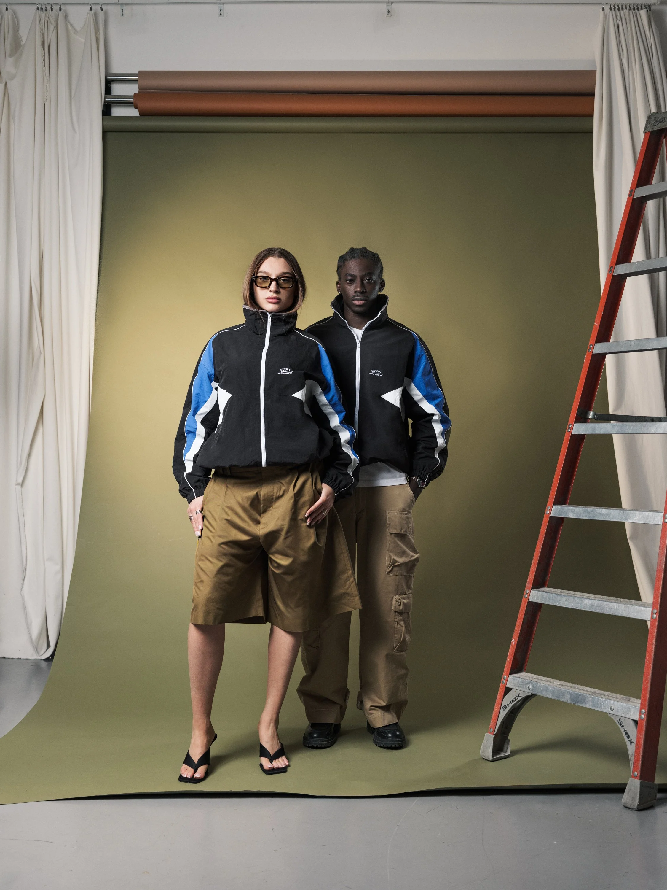 Vanity Apparel advertising image with two models wearing black and blue jackets in studio