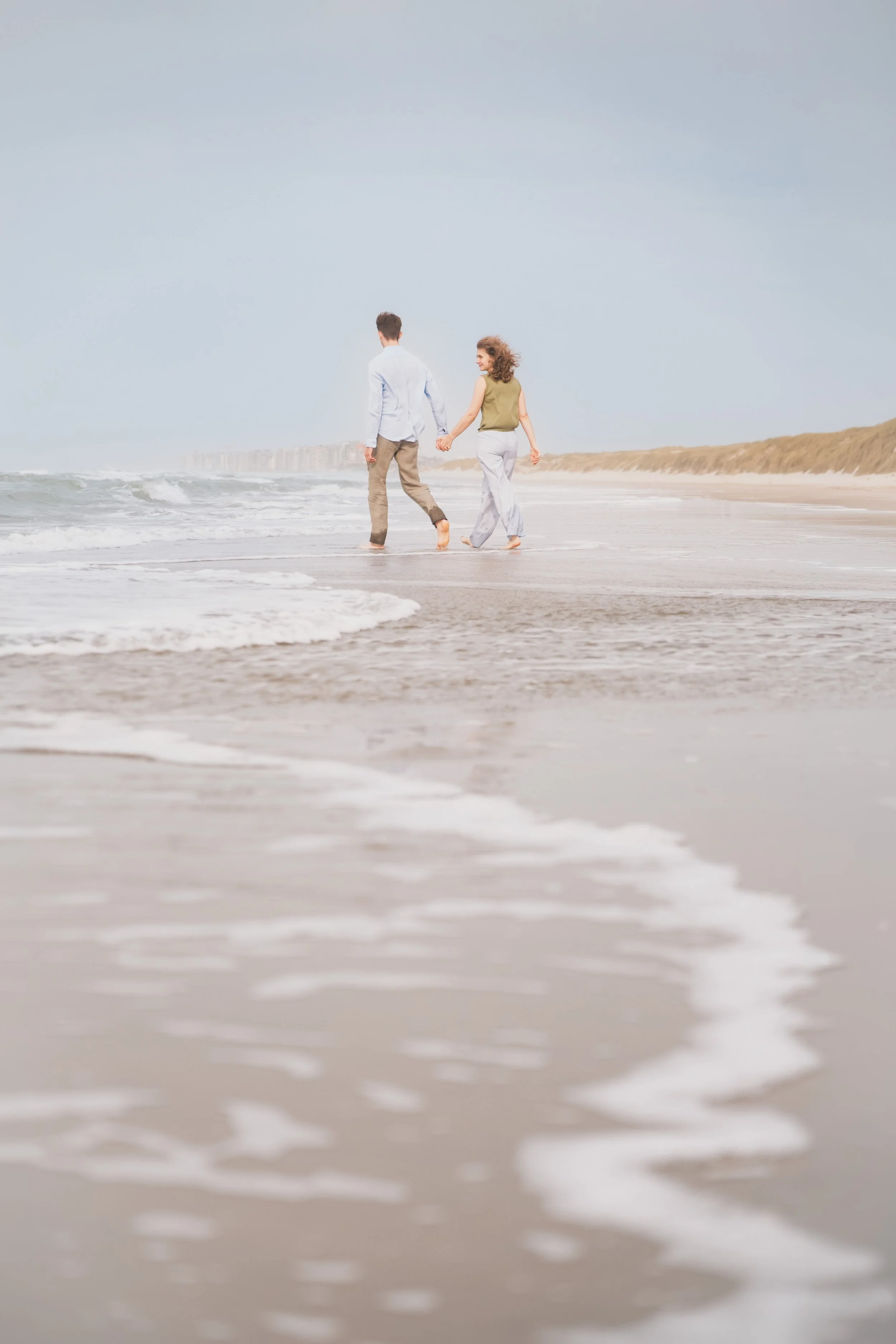 Couple marchant au loin sur une grande plage, photographie de couple atmosphérique en Belgique, Marion David photographe