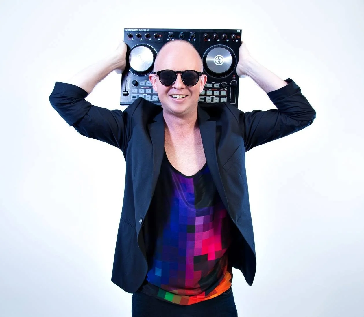 Simon Rooke smiling in sunglasses and a black blazer, holding DJ decks behind his head