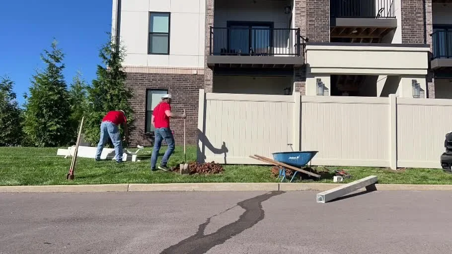 Tan vinyl privacy fence installation separating apartments from a bank parking lot in Wentzville, Missouri