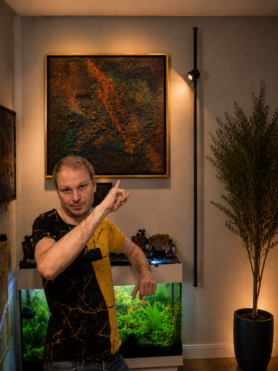 Markus Willems mit dem Original Das geheime Sediment unter der Erosion – Größenvergleich des 50 × 50 cm Mixed-Media-Werks im goldfarbenen Schattenfugenrahmen