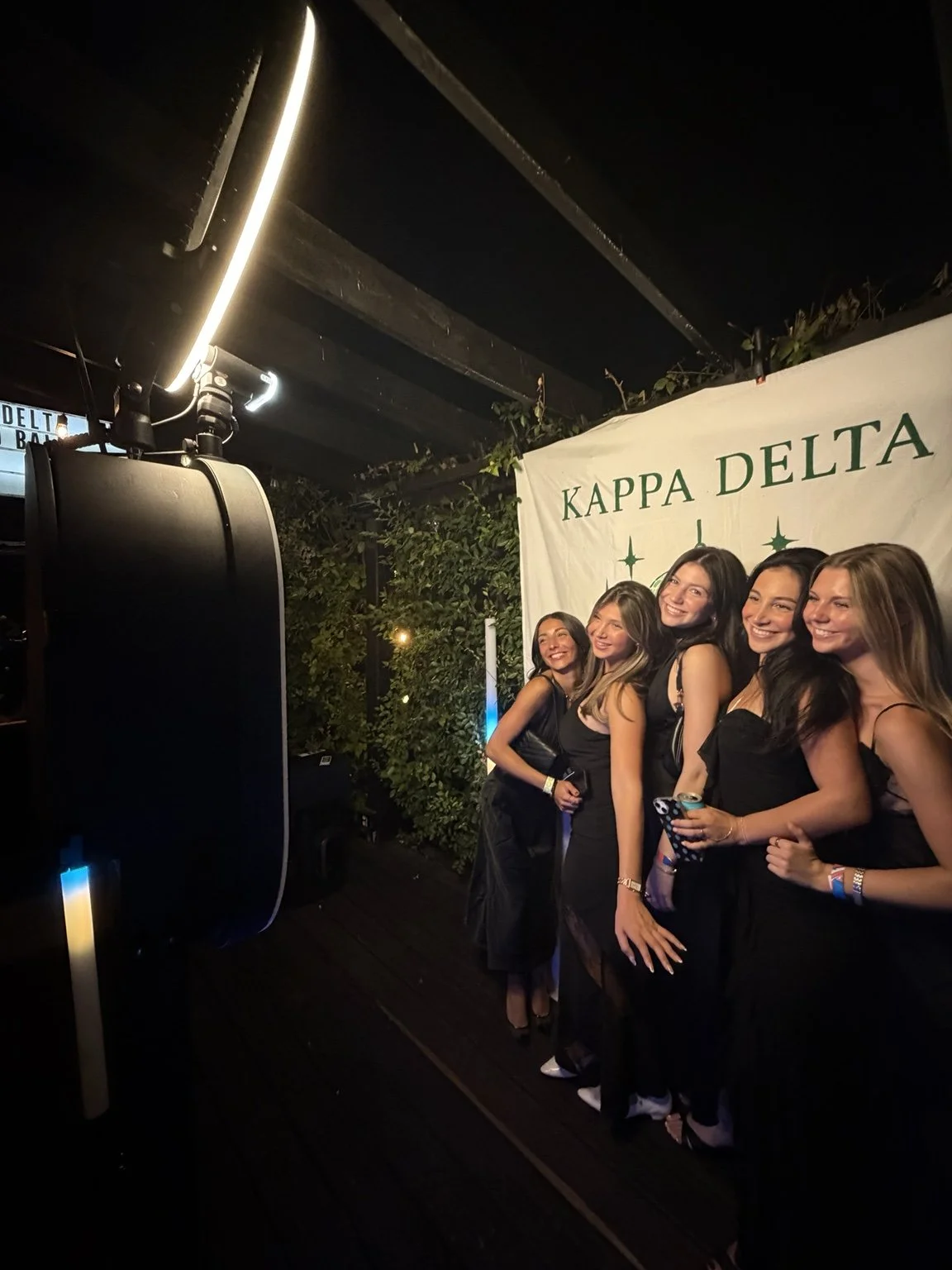 Five guests posing in front of the Kappa Delta backdrop beside the photo booth