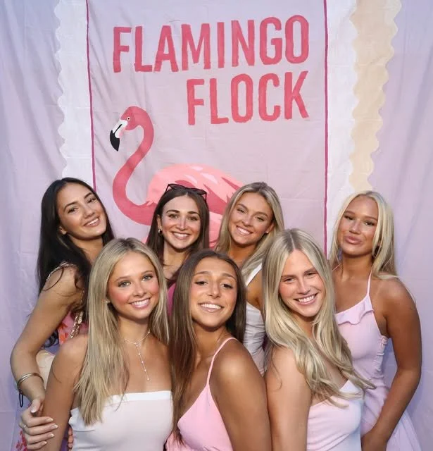 Guests smiling in front of a Flamingo Flock themed event backdrop