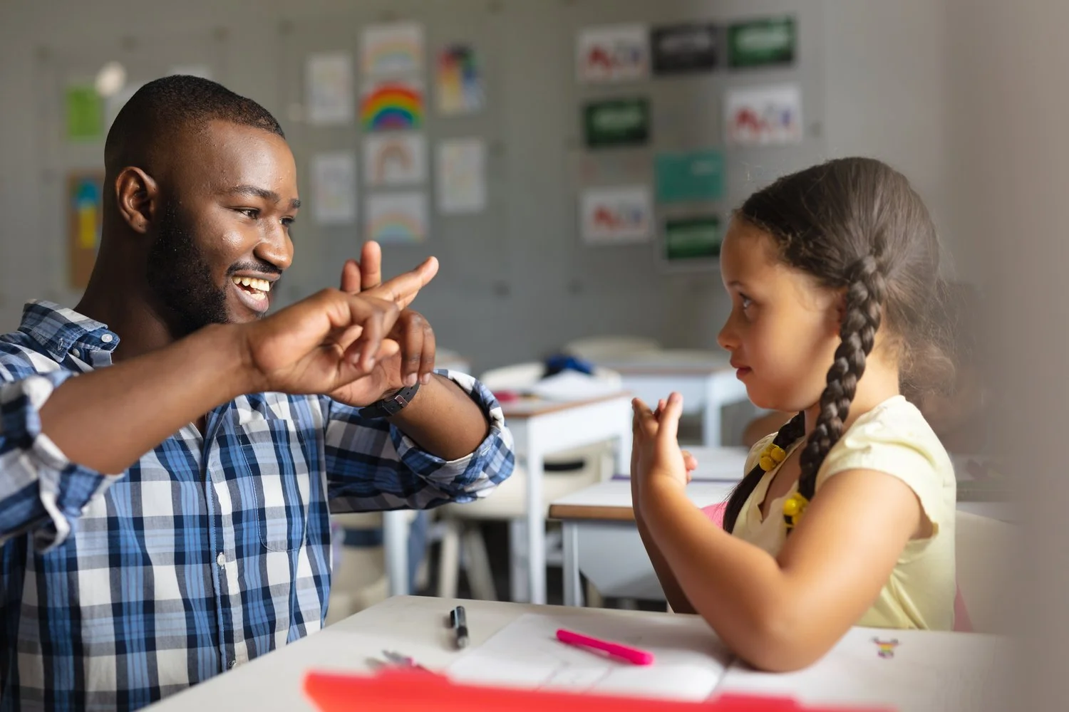 A teacher using sign language with a child in a classroom