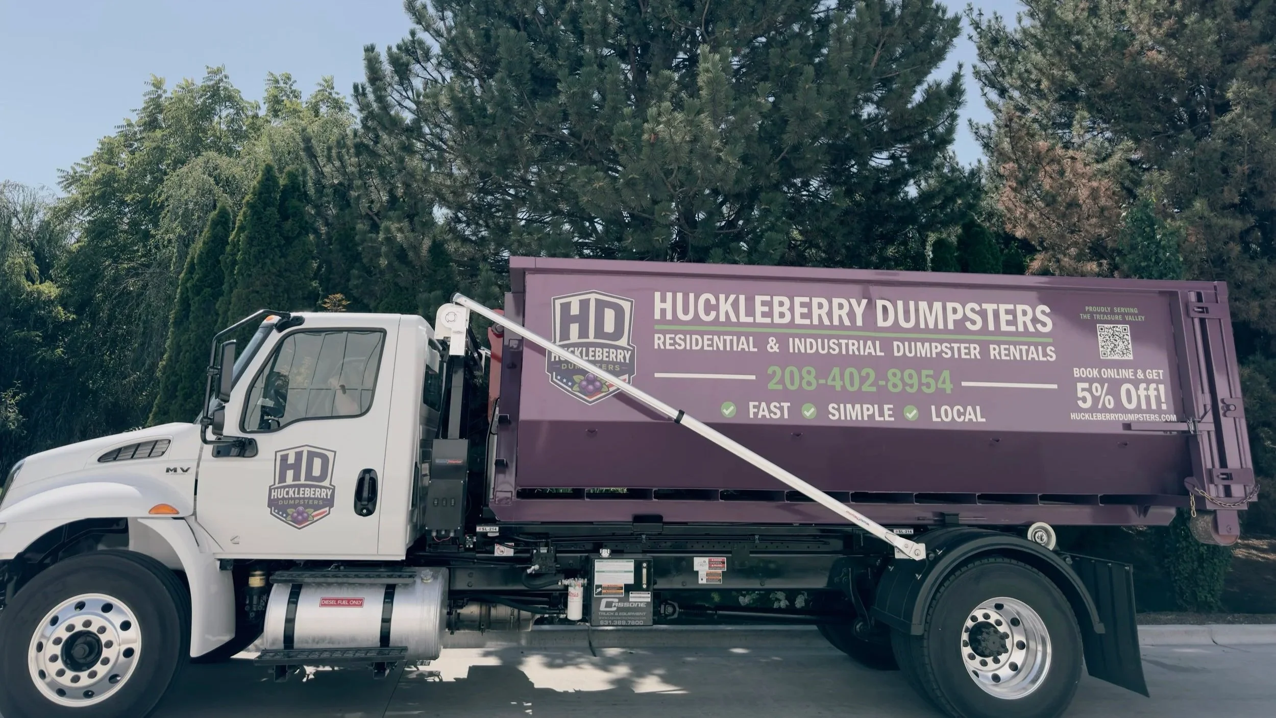 Huckleberry Dumpsters purple dumpster loaded on the company hooklift truck