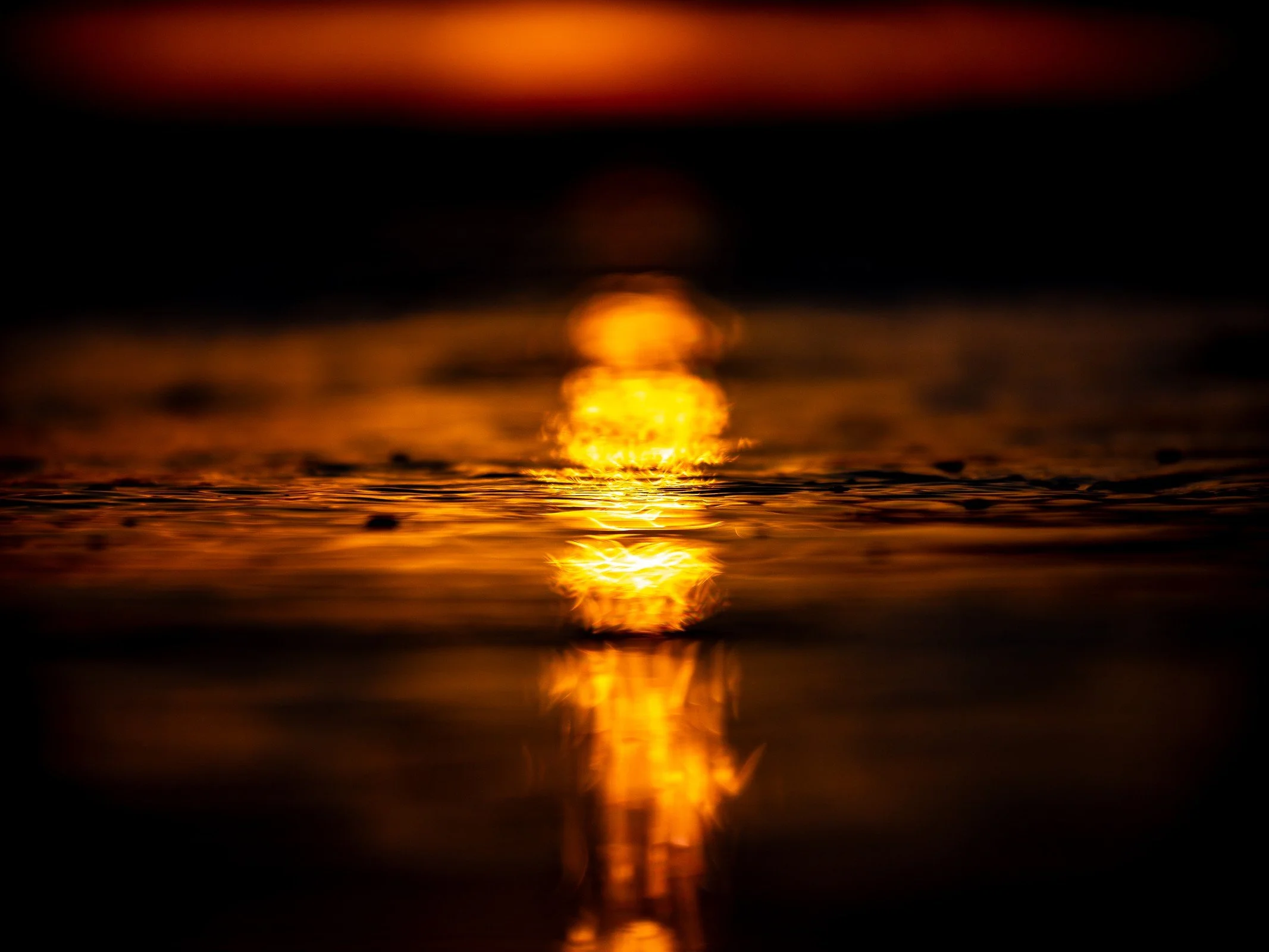 A warm golden reflection on rippled water surrounded by deep shadow.
