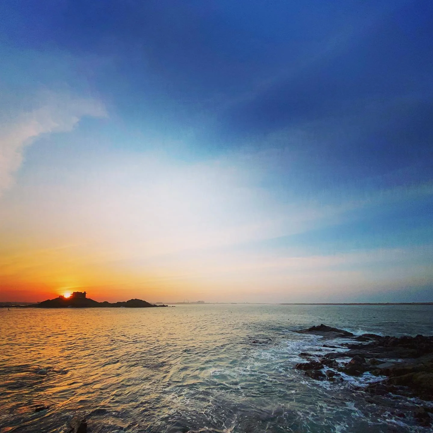 ケンが撮影した、岩礁の小さな社をシルエットに染める海辺の夕日