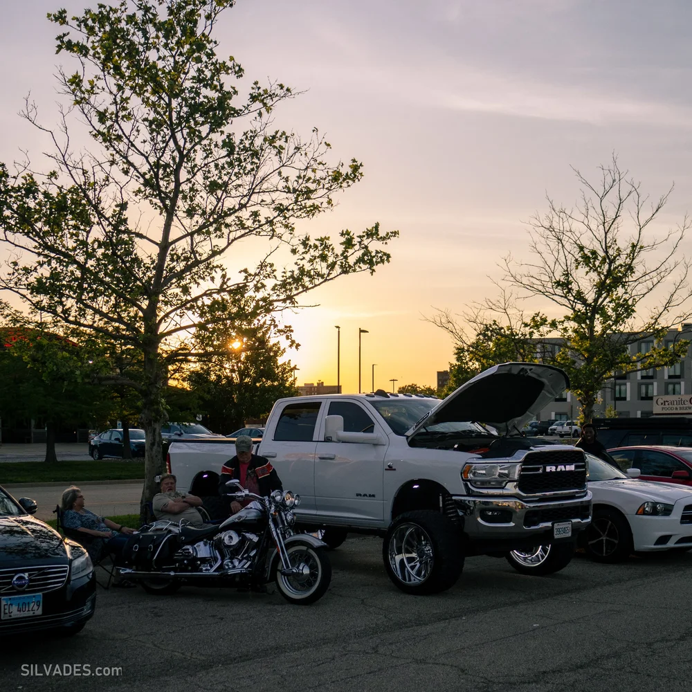Sunset over a car meet with a truck and motorcycle in silhouette