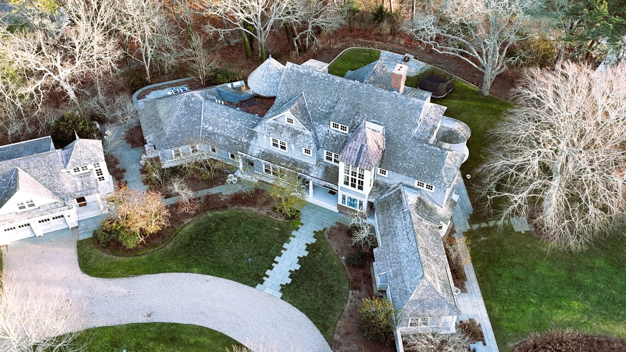 Wide drone view of residential property showing roof geometry, dormers, chimneys, and building massing