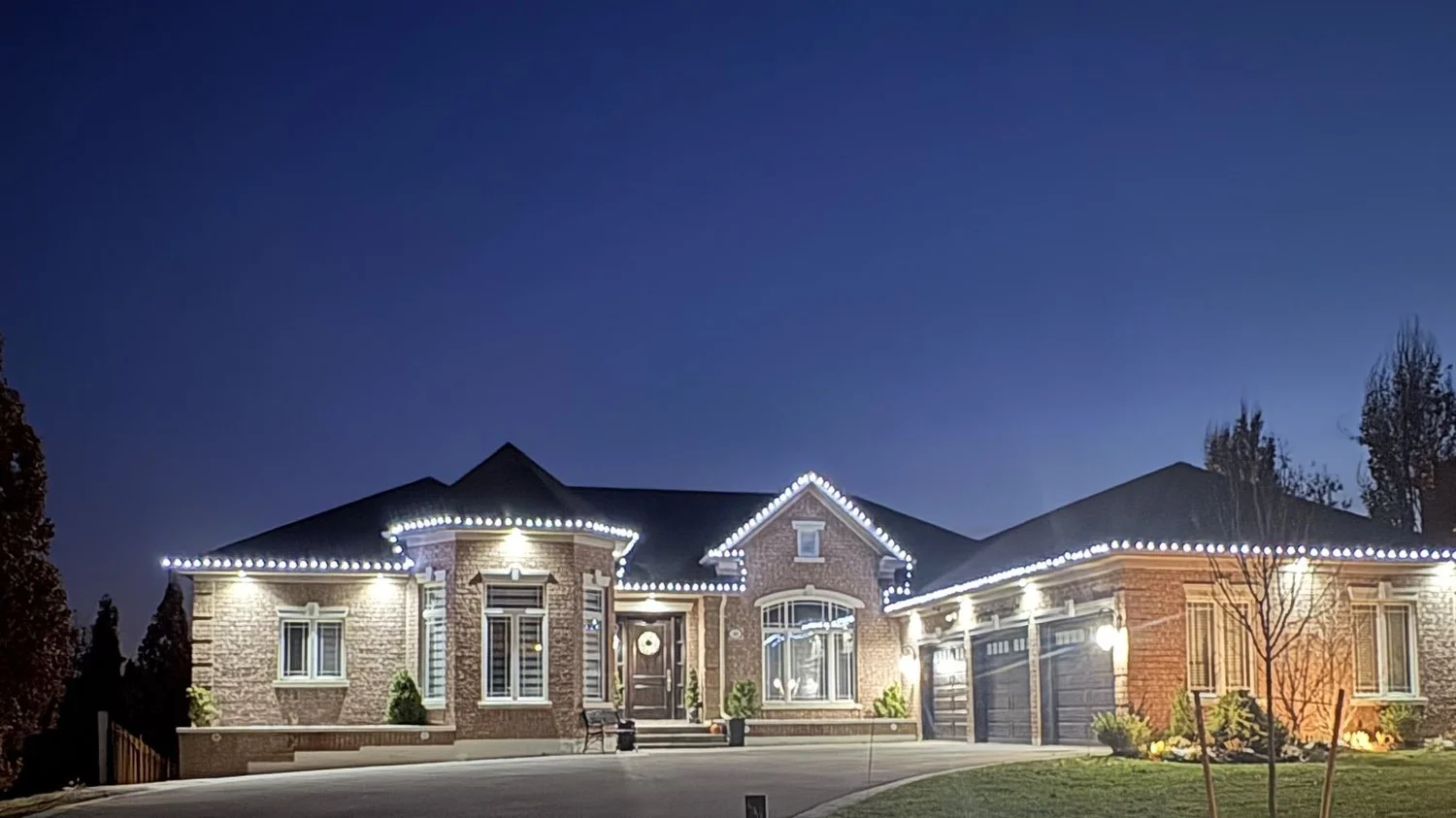 Bungalow with white roofline Christmas lights at dusk, installed by QuickCutz