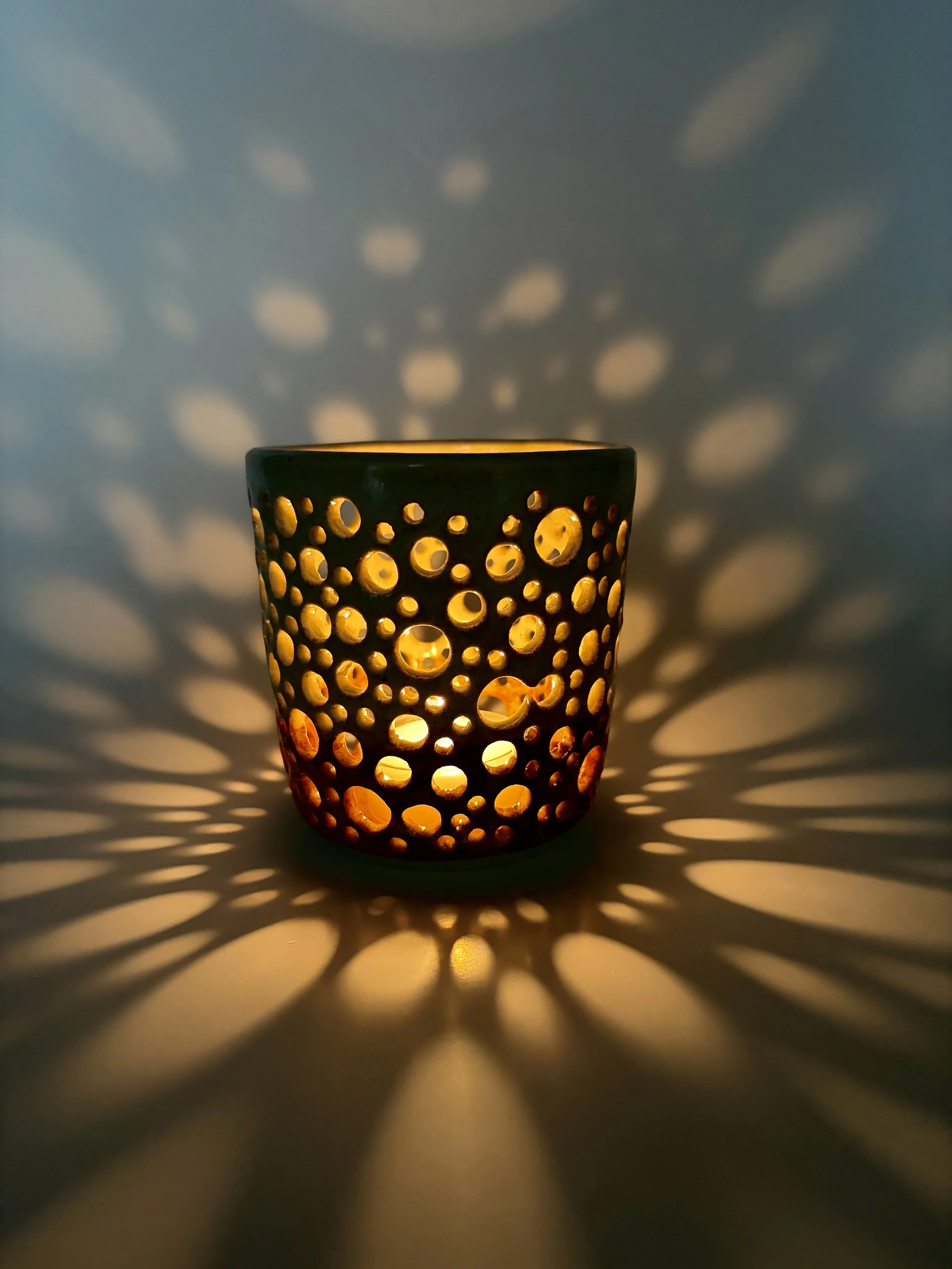 Pierced ceramic lantern casting a pattern of warm light and shadow by Natalie Dahl