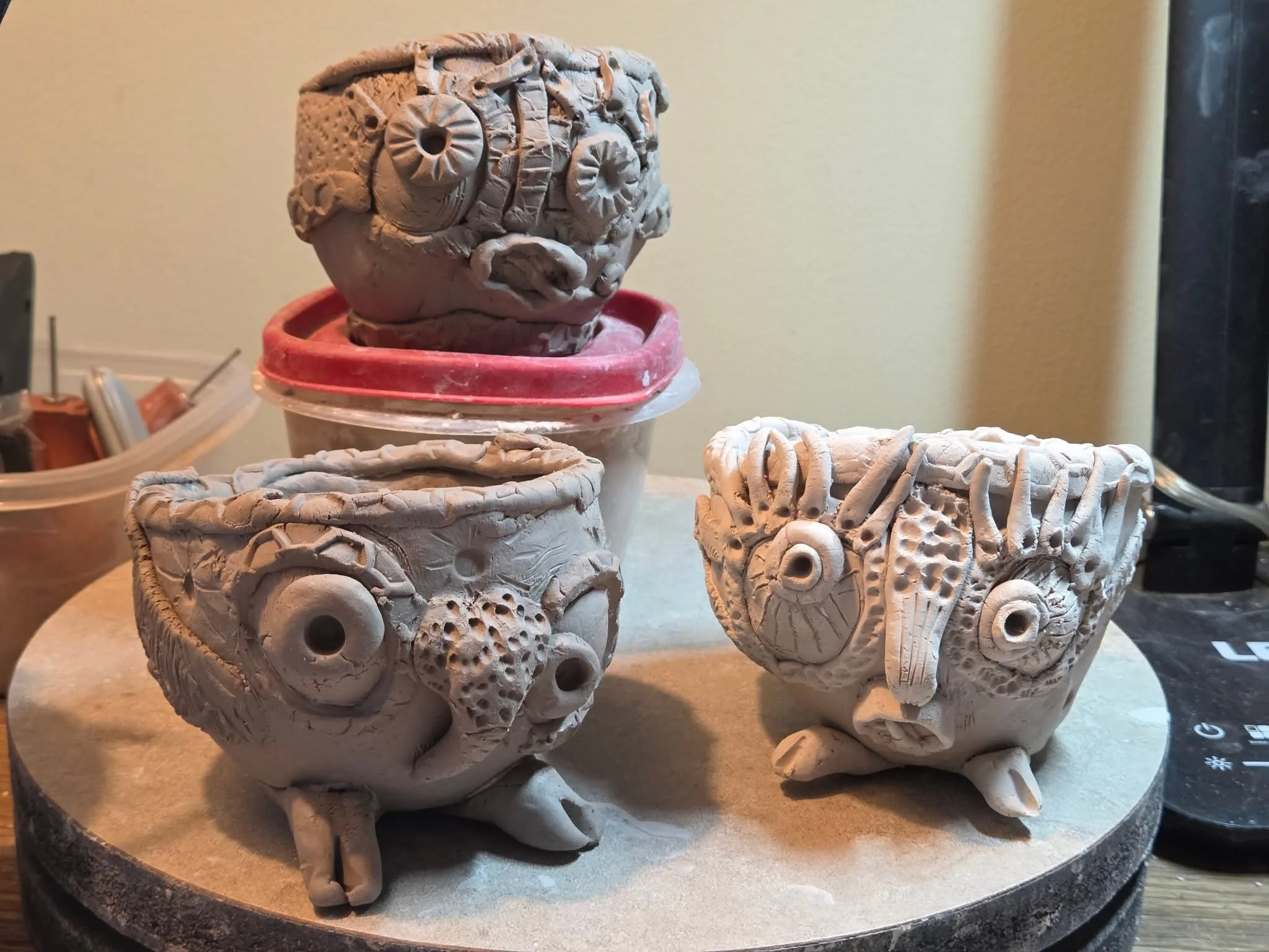 Three unfired handbuilt owl vessels by Moe Lewis-Wolf with layered textures and applied facial features