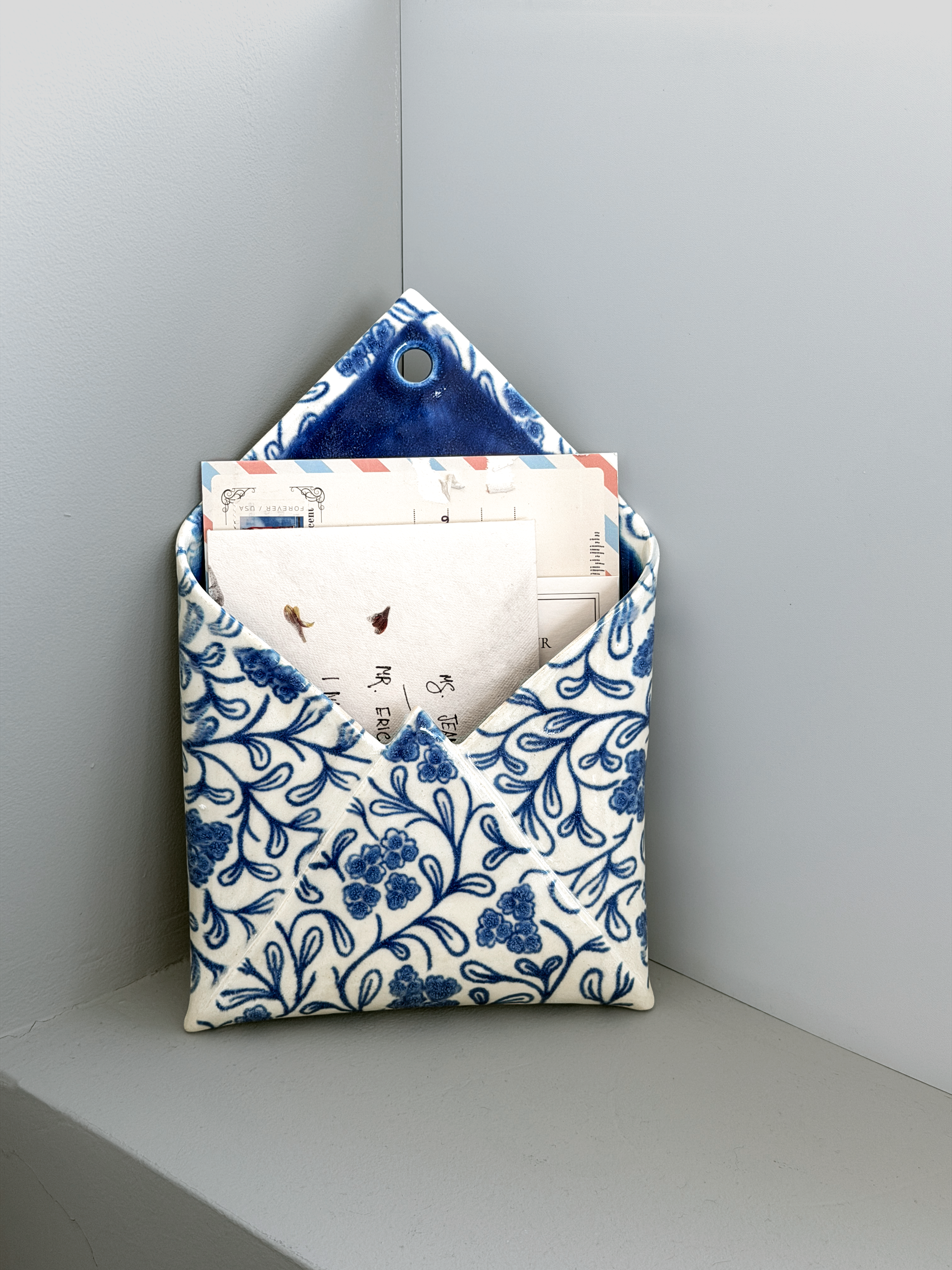 Blue-and-white ceramic wall envelope by Mira Etingof holding letters