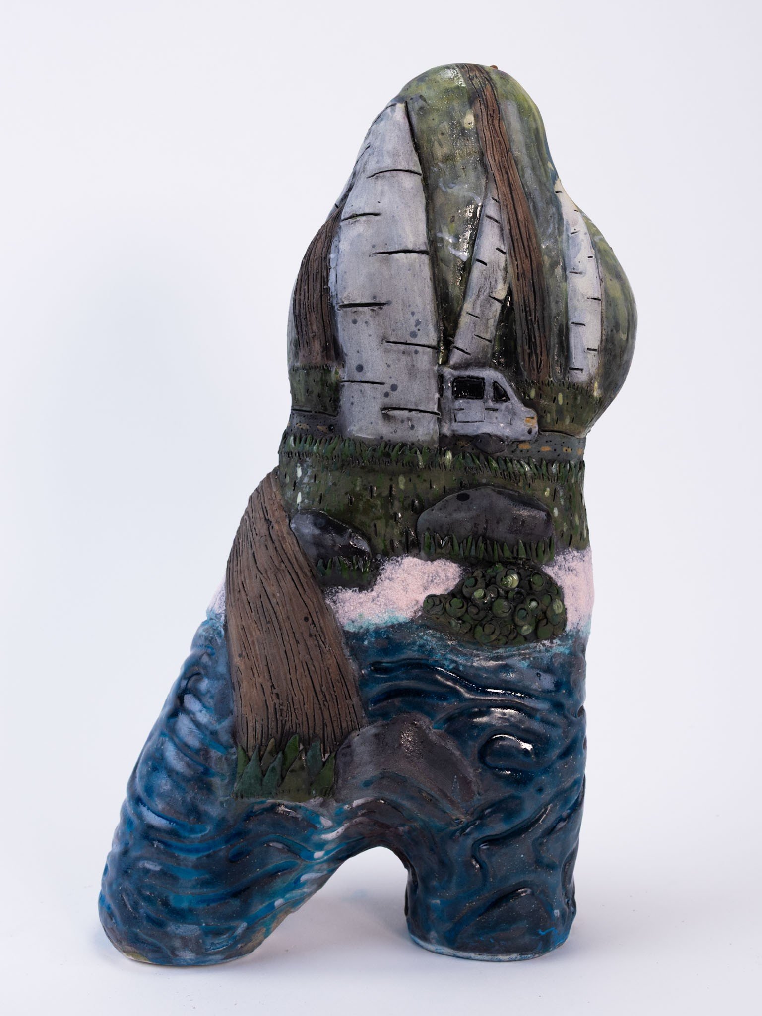 Ceramic sculpture combining a highway, trees, a vehicle, and blue water
