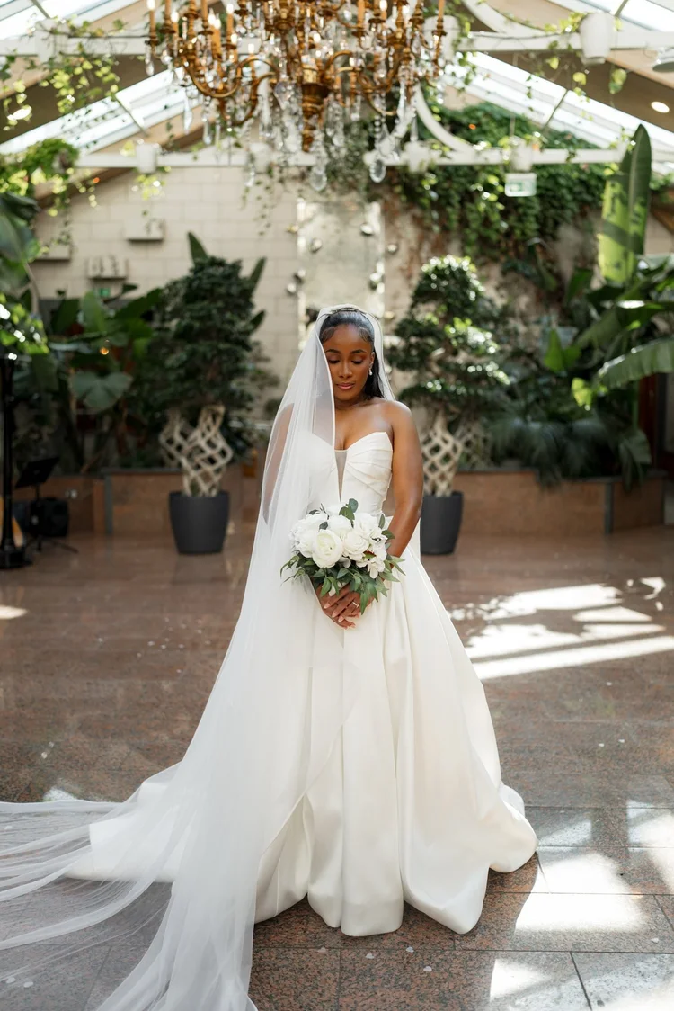 Bridal portrait beneath a chandelier in a glasshouse wedding venue