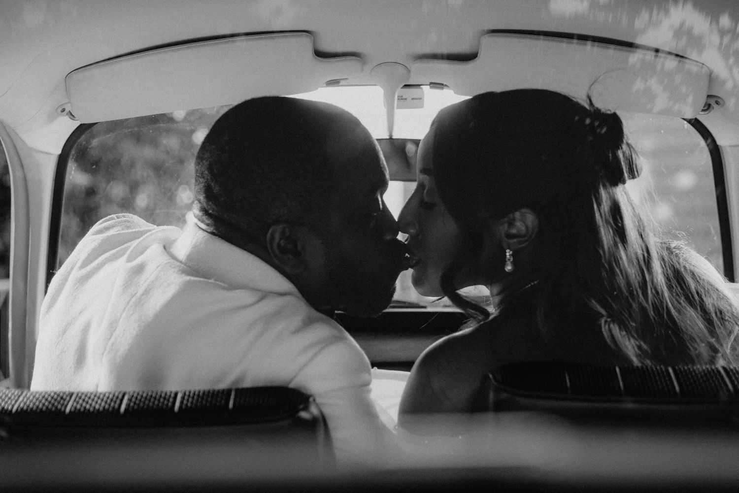 Black and white photograph of newlyweds sharing a kiss in the back of their wedding car