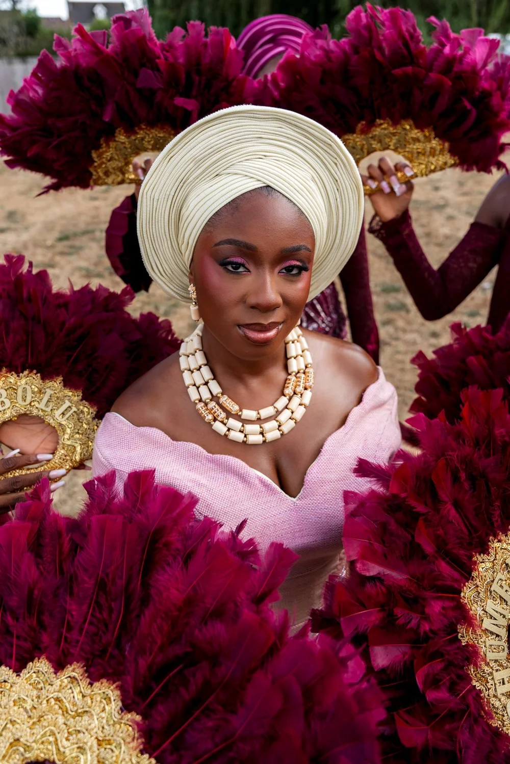 Bride in a gele surrounded by feather fans at a Nigerian traditional wedding