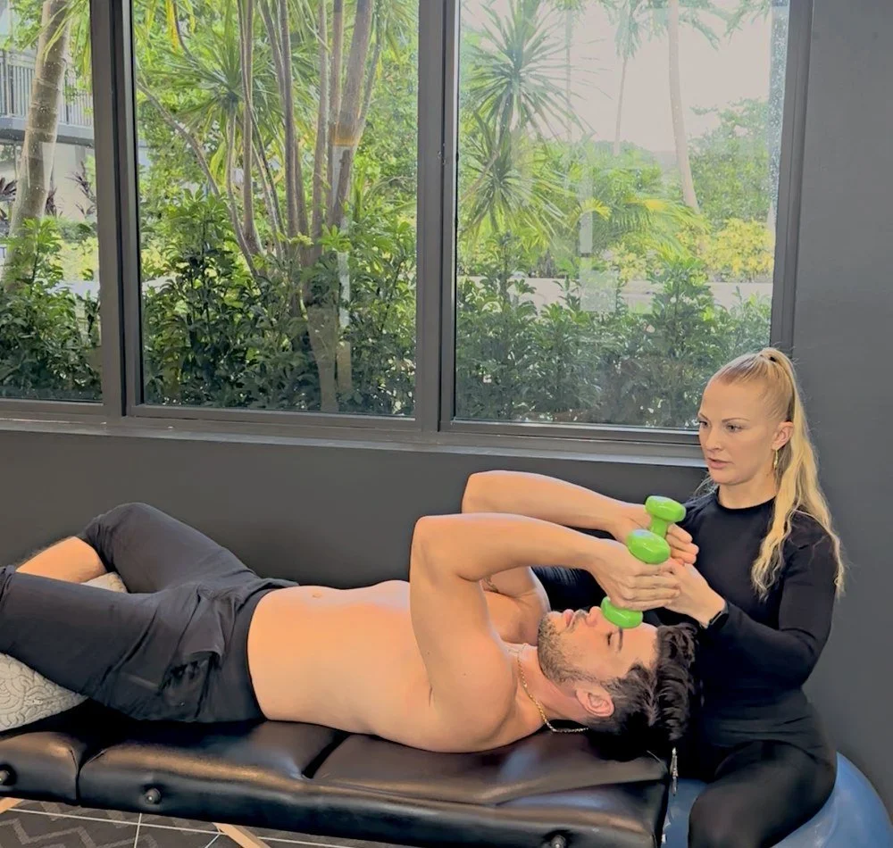 Dr. Karla Kane guiding a patient through a supine dumbbell shoulder exercise