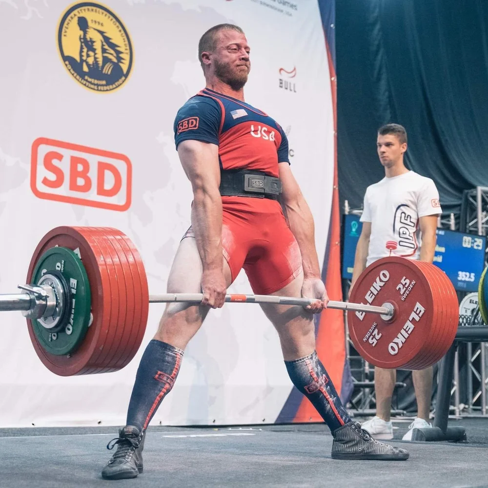 David Woolson pulling a deadlift in a Team USA singlet at an IPF competition, 2019