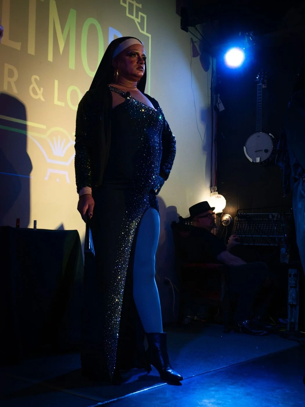 Sister Anita in a sparkling dark gown and black veil, standing full length on a stage.