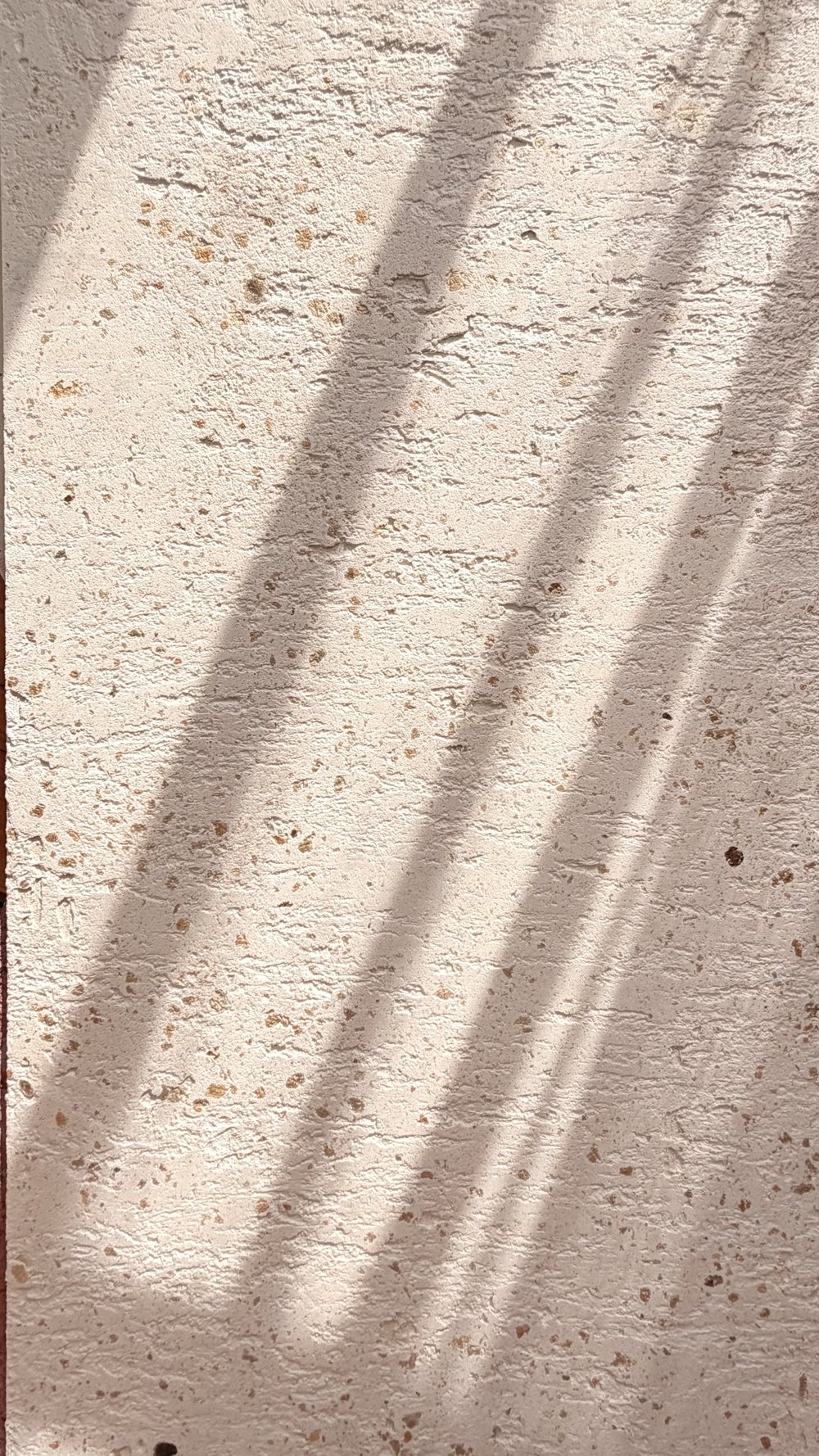 Pale textured plaster with small surface indentations and soft diagonal shadows