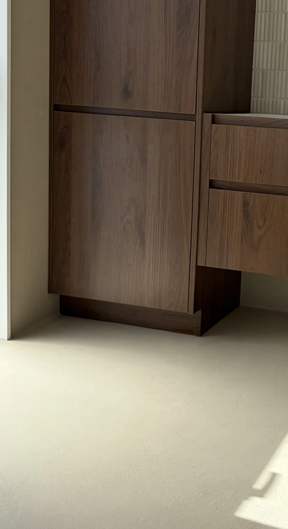 Light microcement floor meeting dark timber bathroom cabinetry